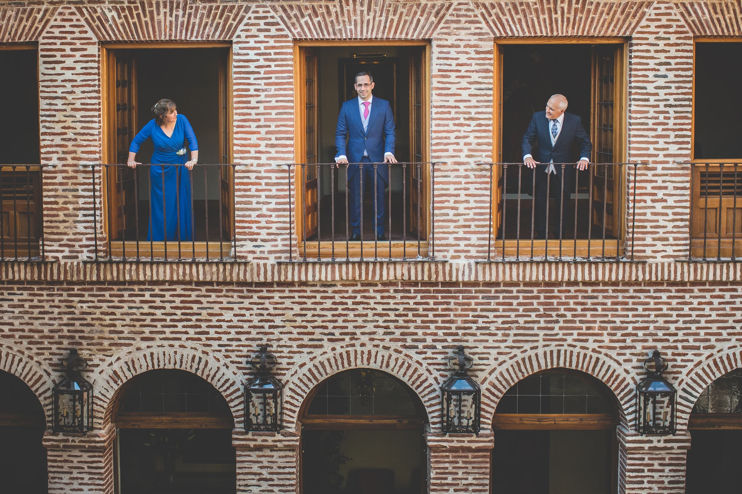 Novio con familiares asomados a los balcones del patio de ladrillo.
