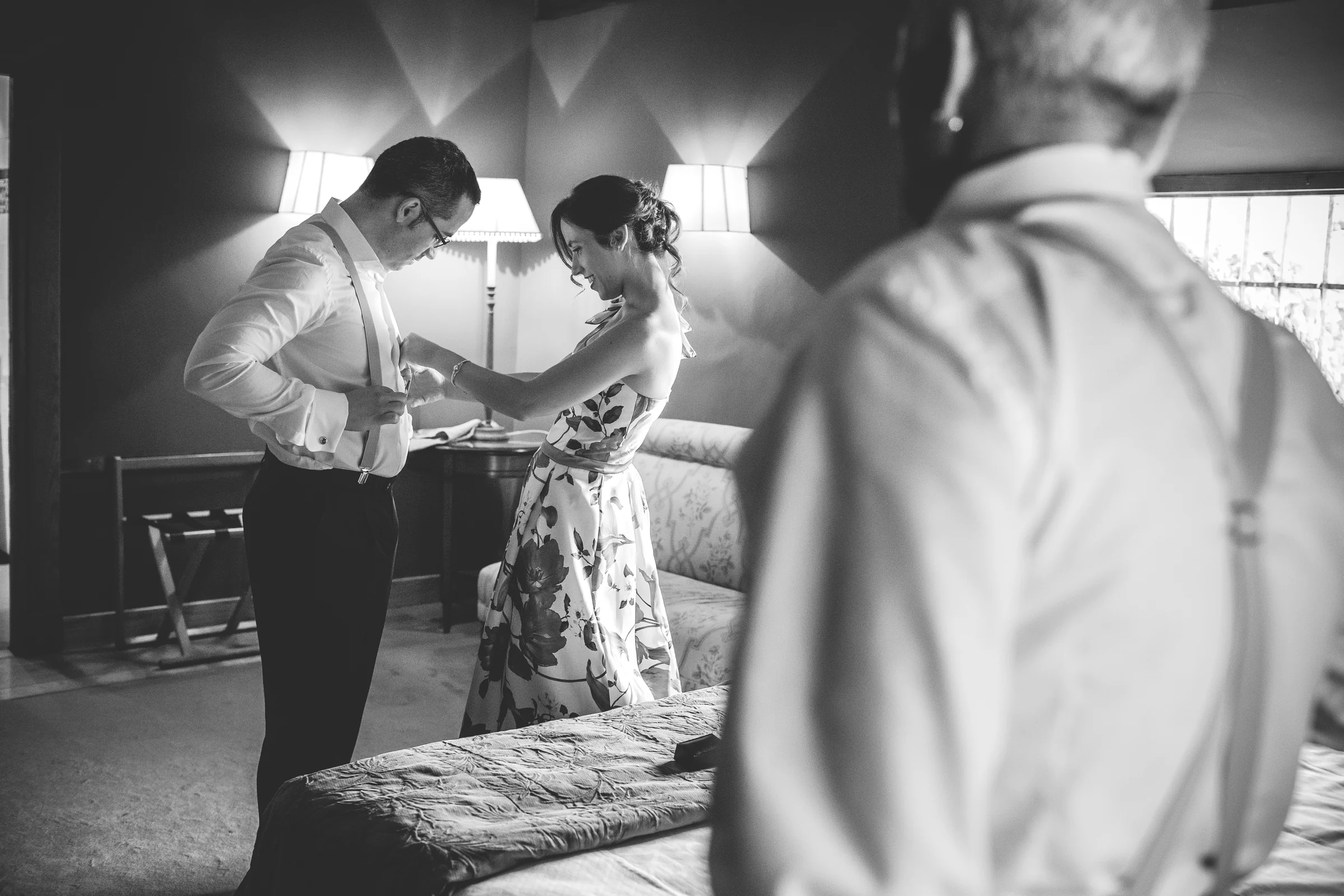 Novio terminando de colocarse la ropa con ayuda de una acompañante en blanco y negro.
