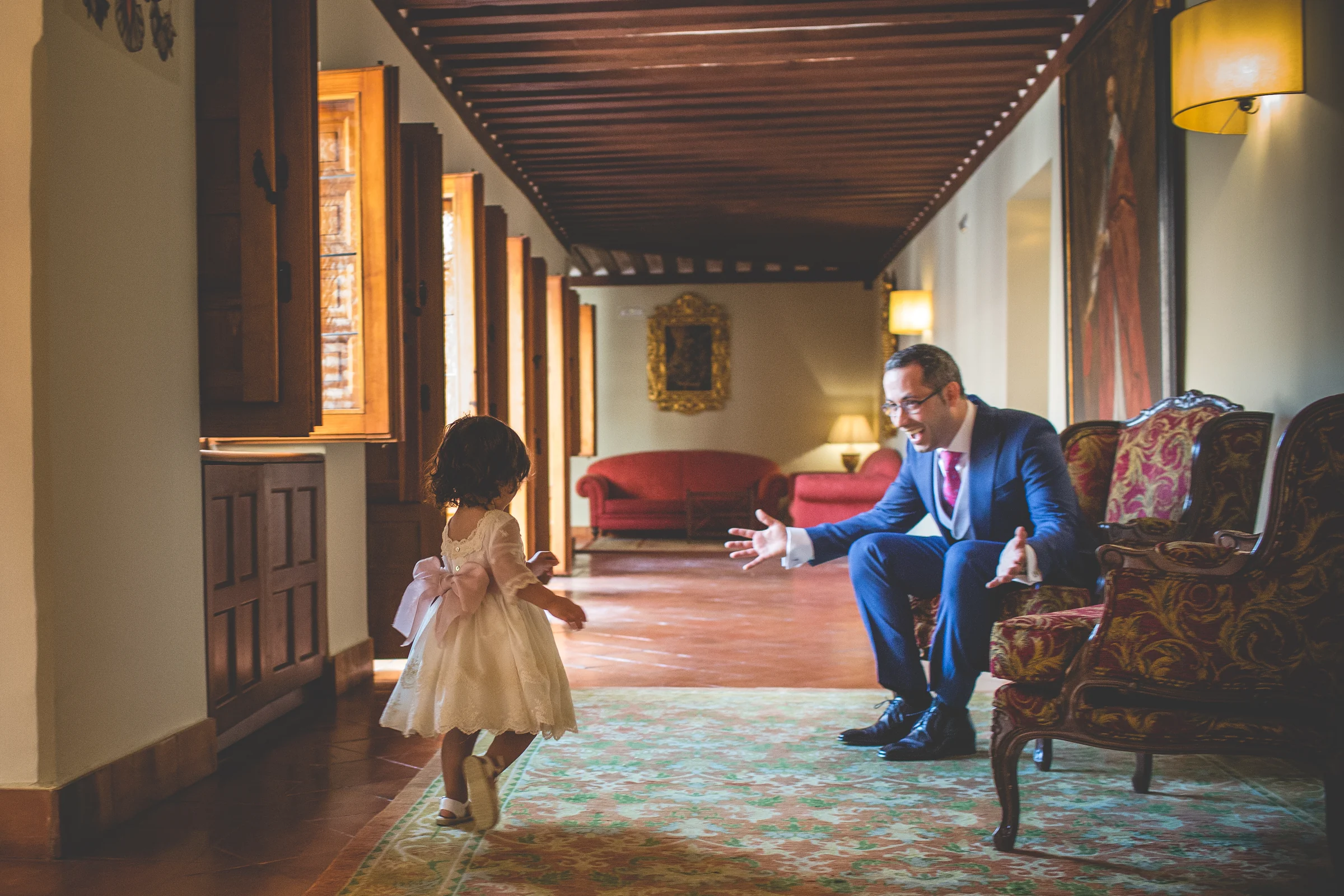 Novio recibiendo a una niña que corre hacia él por un pasillo interior.