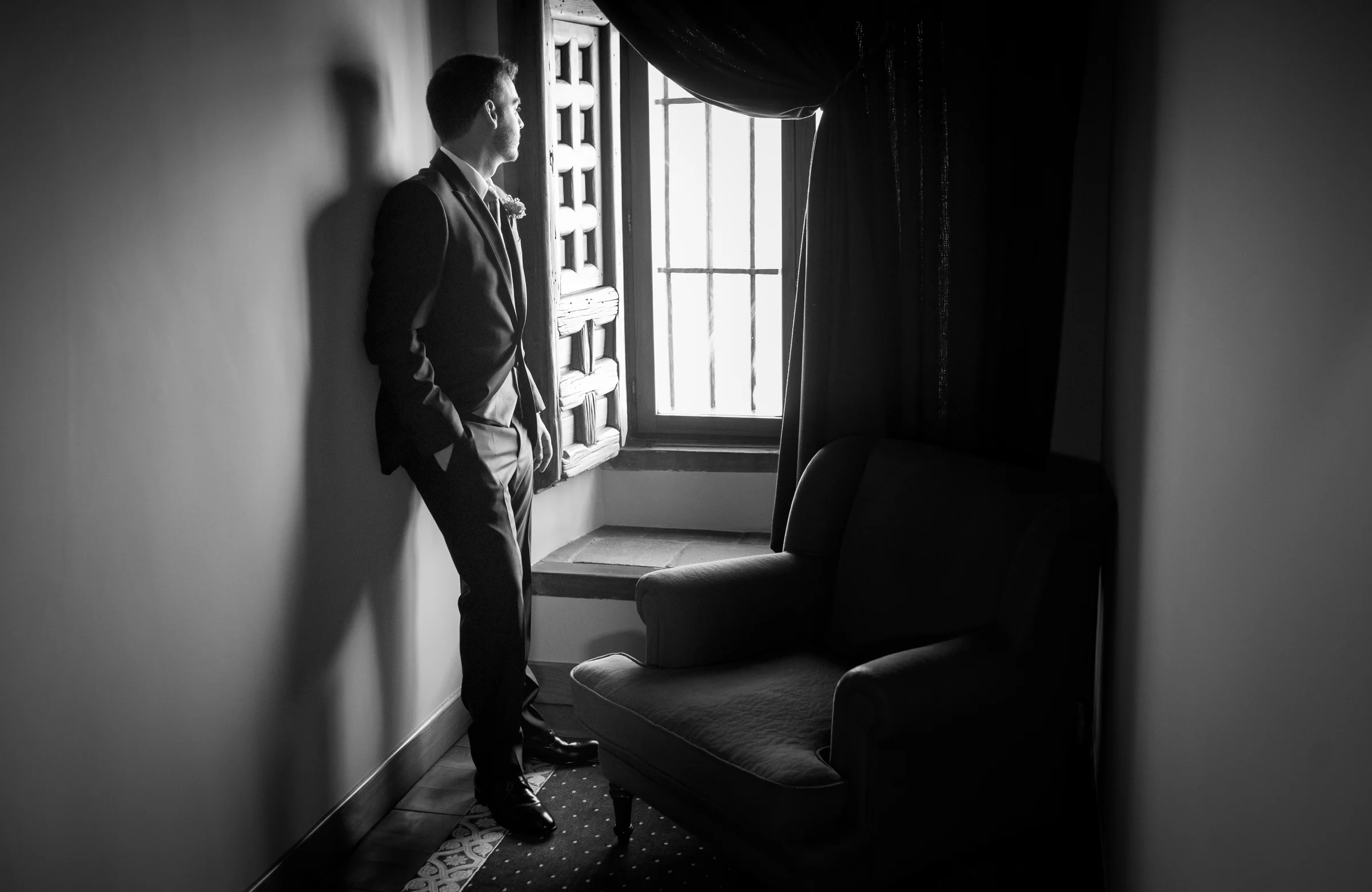 Novio mirando por una ventana en una fotografía en blanco y negro.