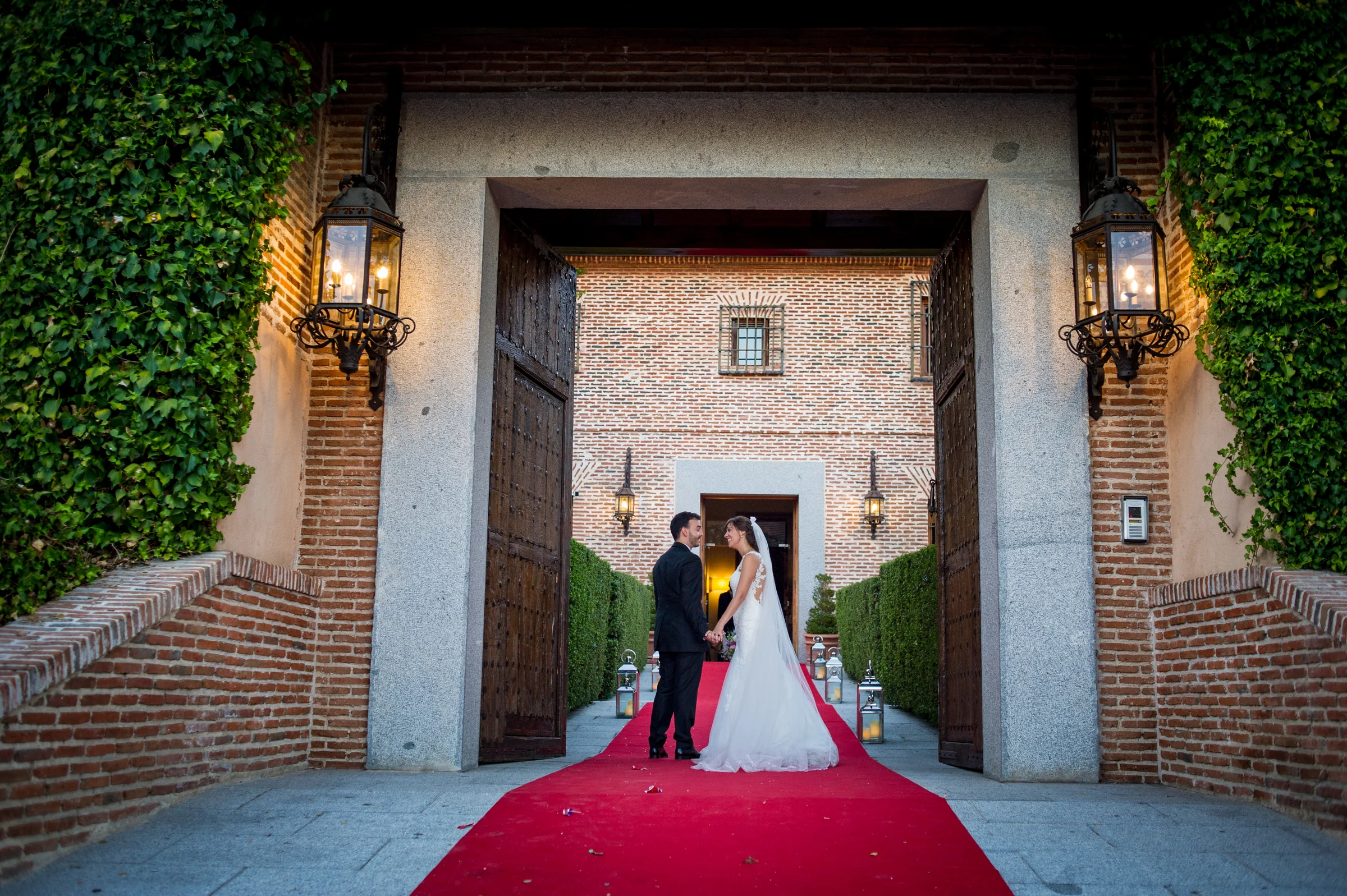 Pareja de novios sobre una alfombra roja bajo el gran acceso de ladrillo.