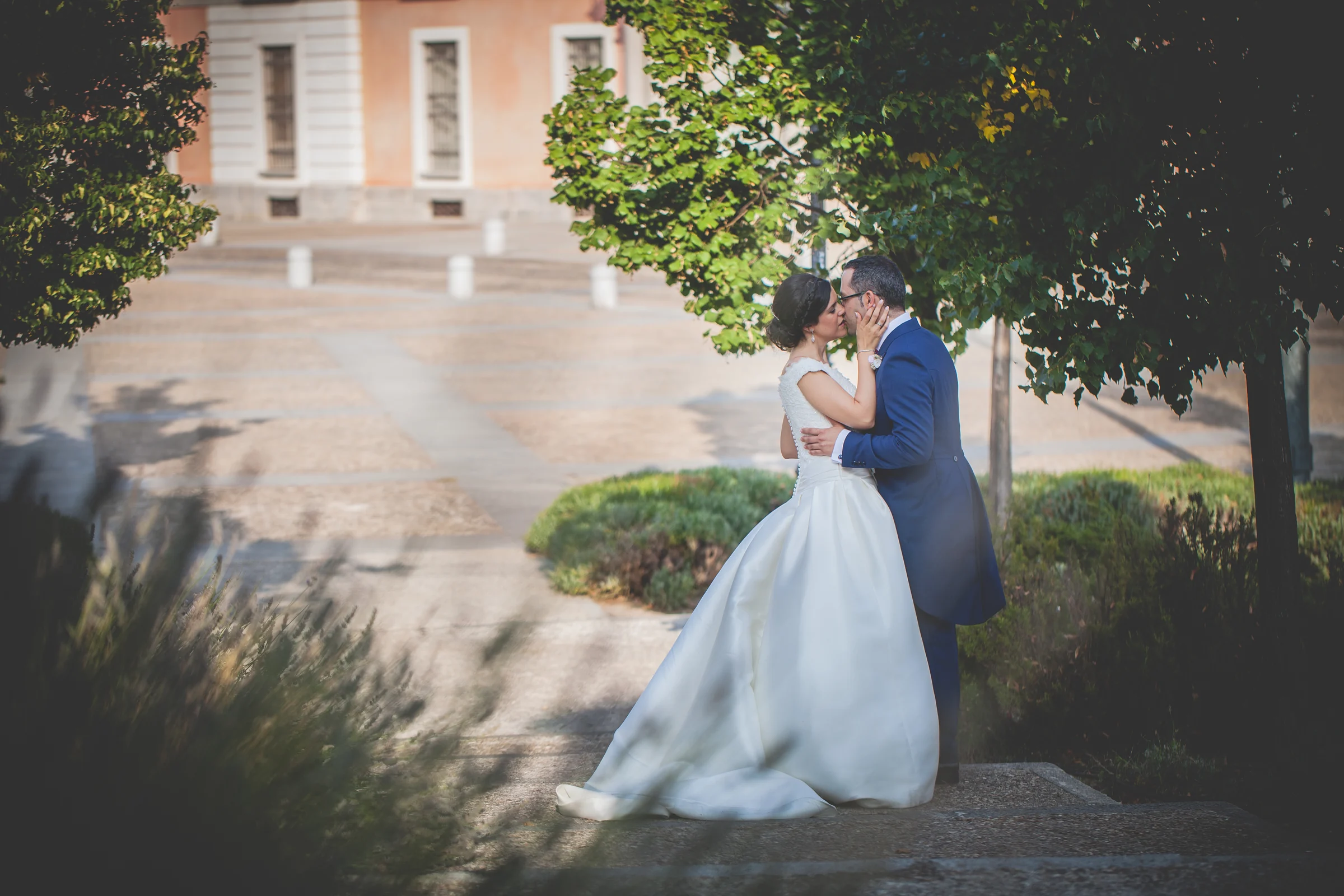 Pareja de novios besándose bajo un árbol durante la sesión exterior.