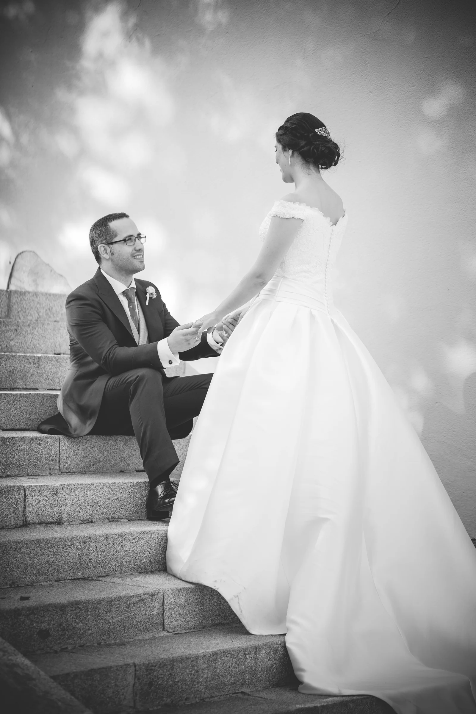 Novio sentado en una escalera tomando las manos de la novia en blanco y negro.