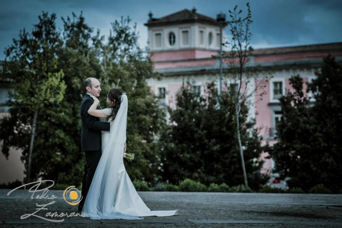 Pareja de novios abrazada con el palacio rosado al fondo en Boadilla del Monte.