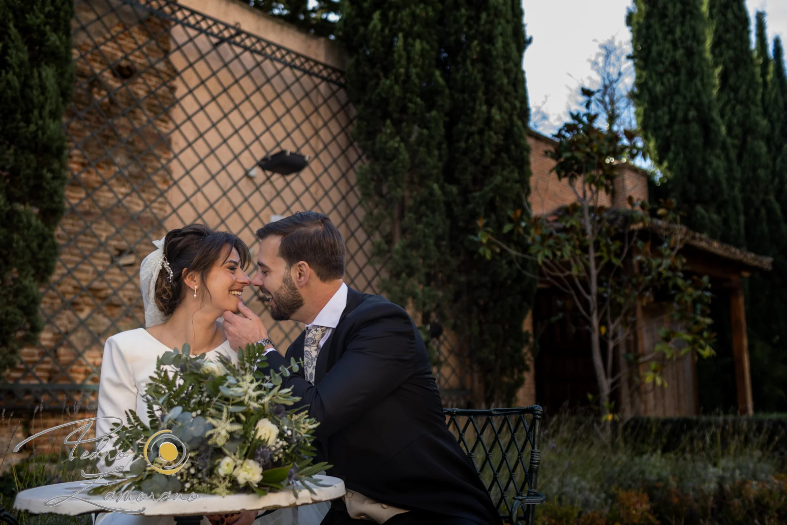 Pareja de novios sentada y sonriendo en un rincón del jardín.