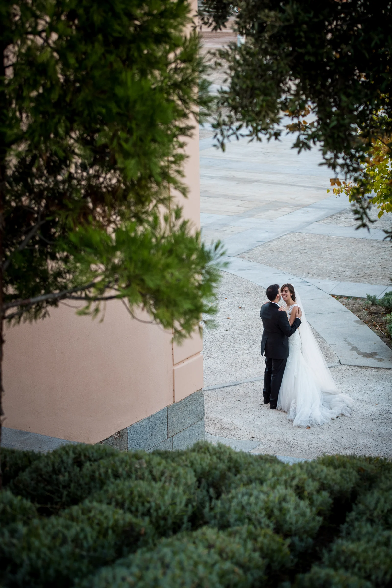 Pareja de novios vista a distancia entre árboles y jardines.