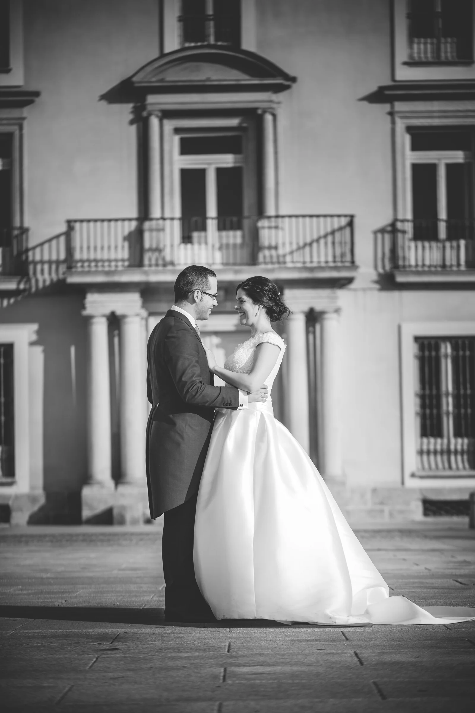 Pareja de novios abrazada frente al palacio en una fotografía en blanco y negro.