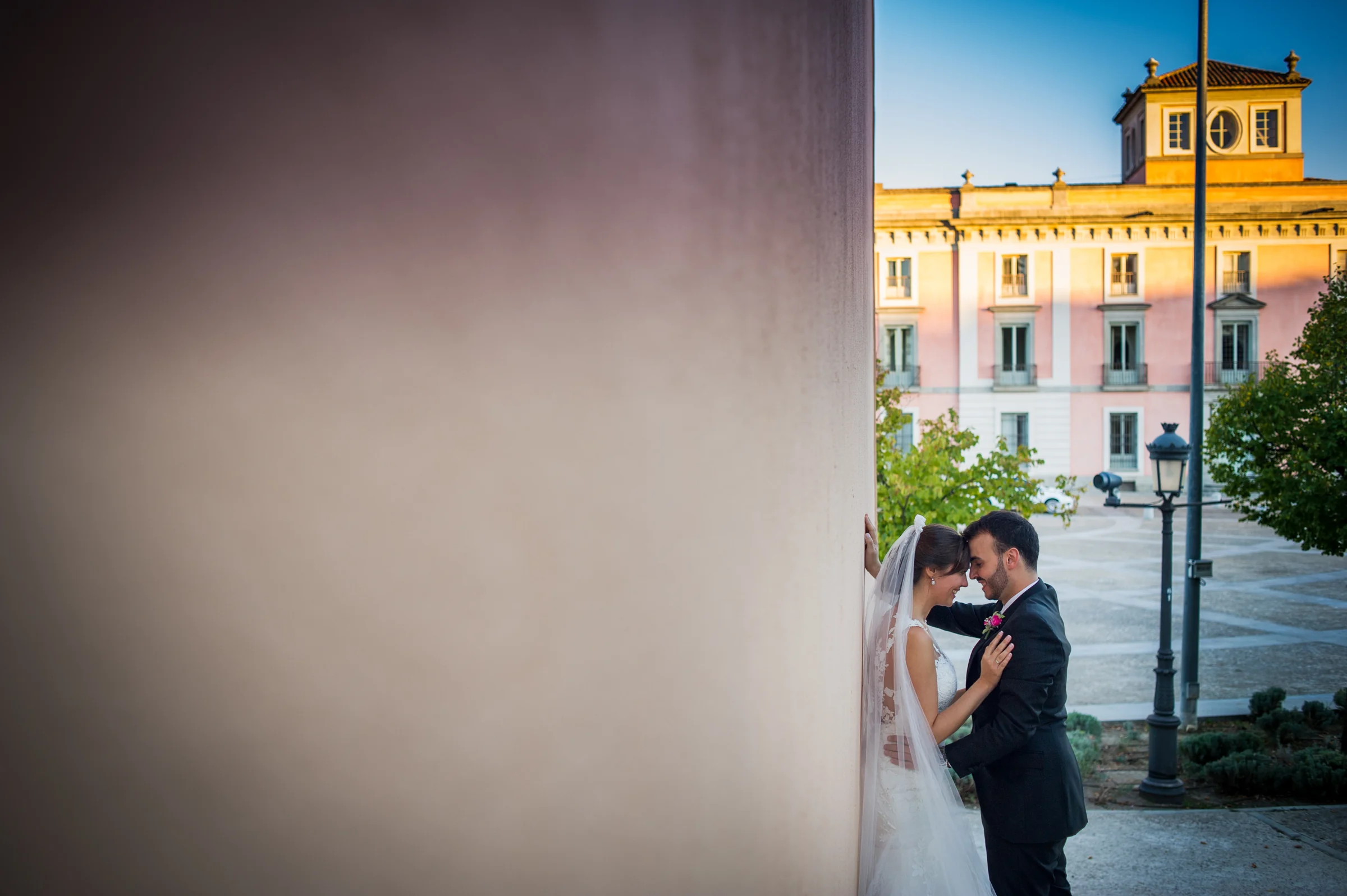 Pareja de novios enmarcada por un muro con el palacio de Boadilla al fondo.