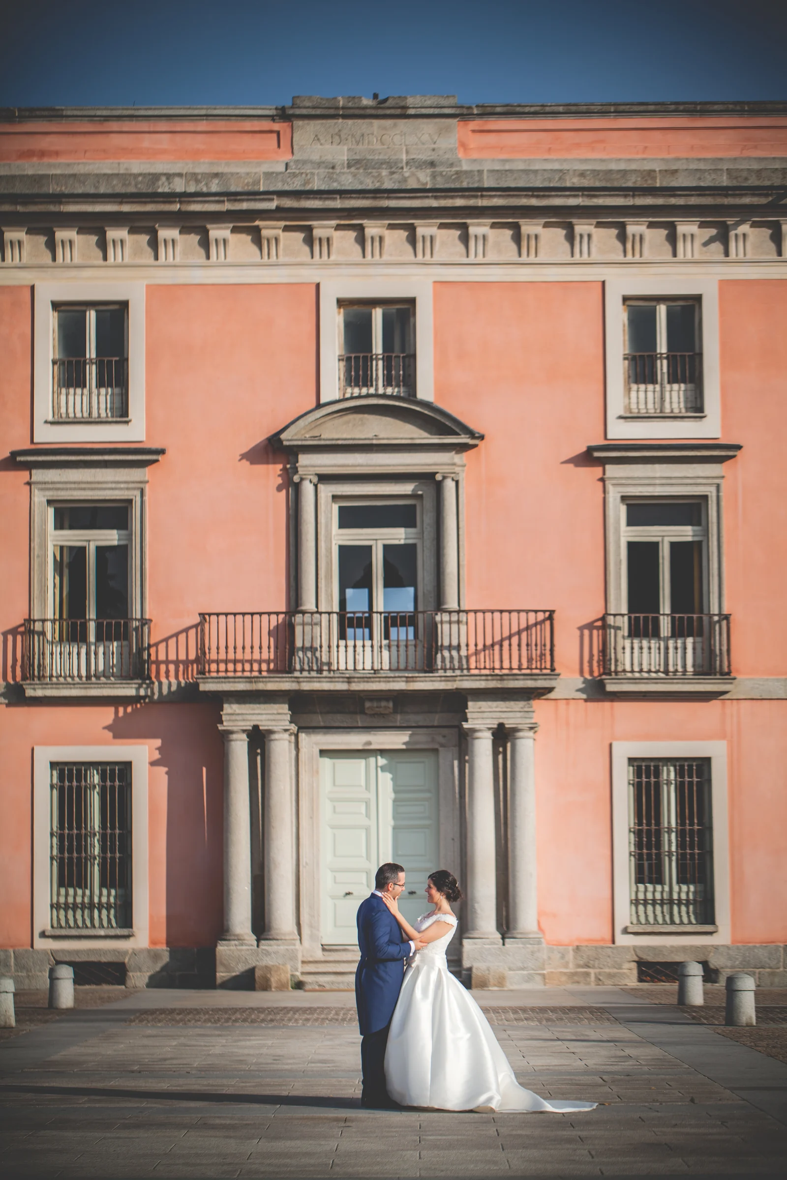 Pareja de novios posando frente a la fachada rosada del palacio de Boadilla del Monte.