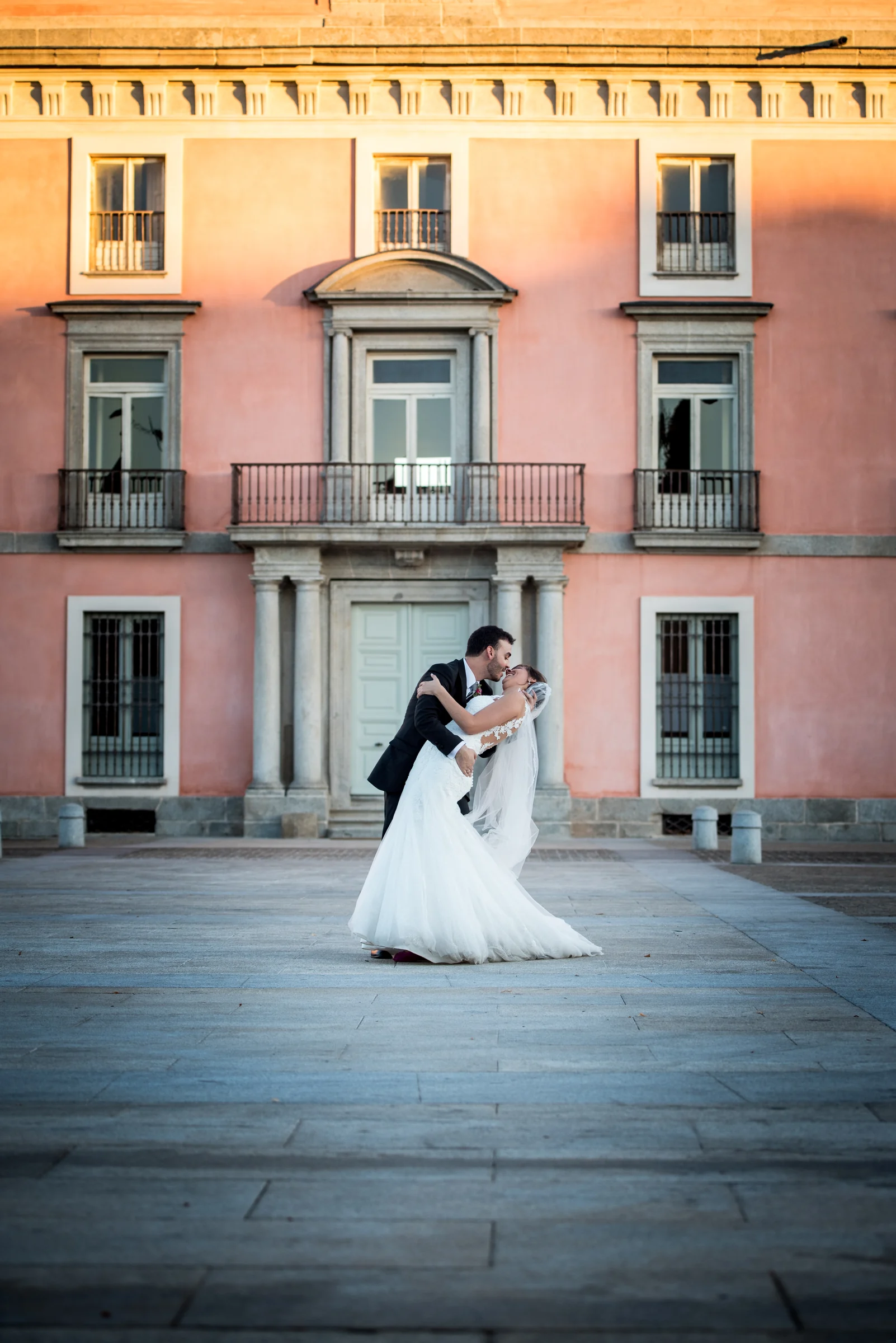 Pareja de novios besándose frente al palacio de Boadilla del Monte en formato vertical.