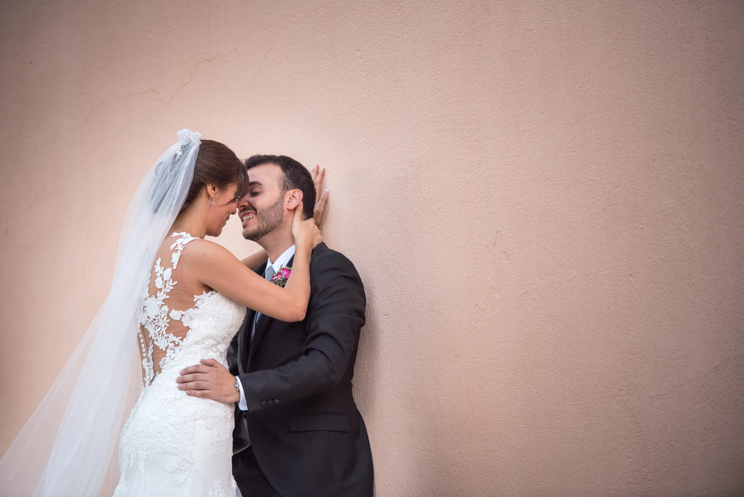 Pareja de novios abrazada junto a un muro rosado durante la sesión de boda.