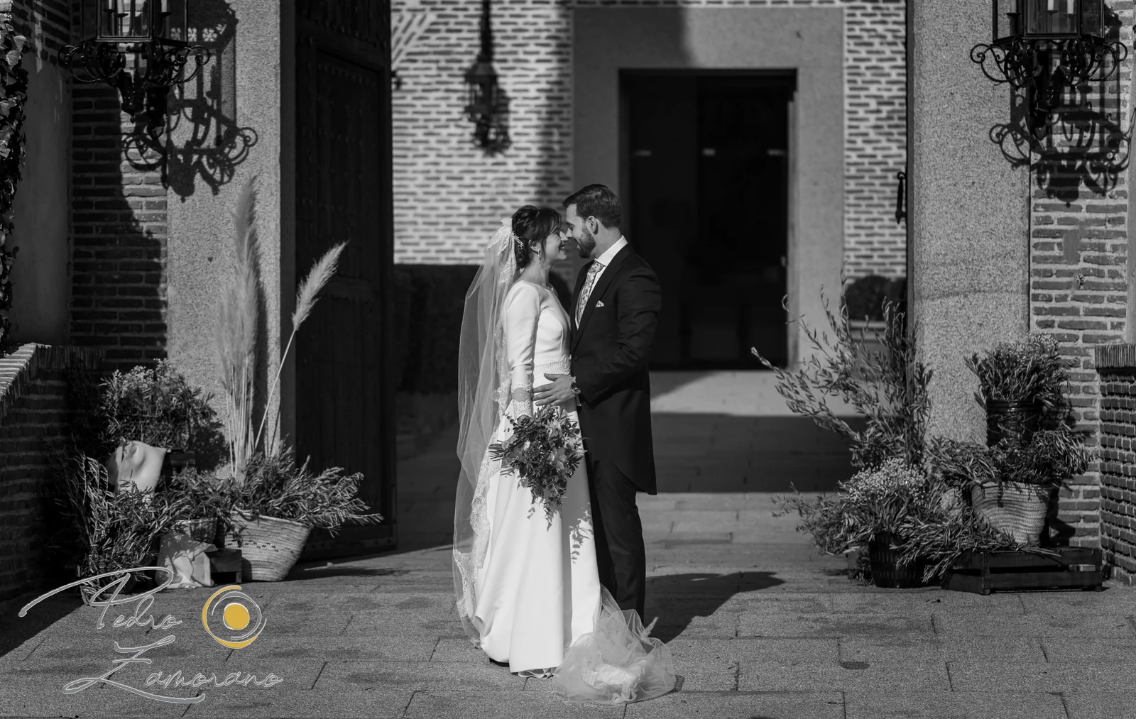 Pareja de recién casados en blanco y negro junto a una entrada de ladrillo.