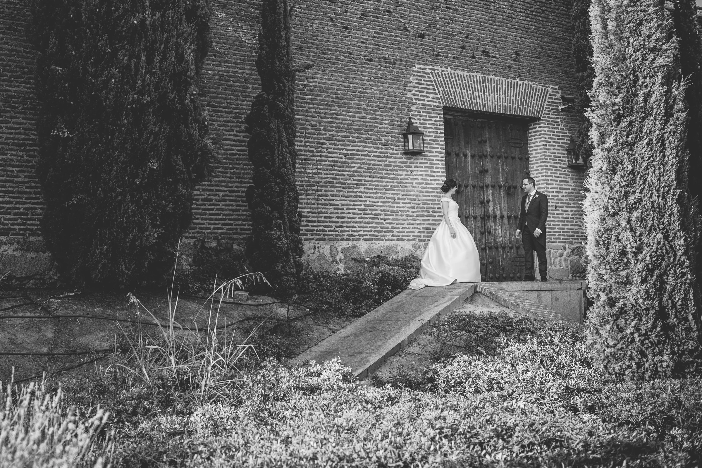 Pareja de novios frente a un portón de ladrillo en una fotografía en blanco y negro.