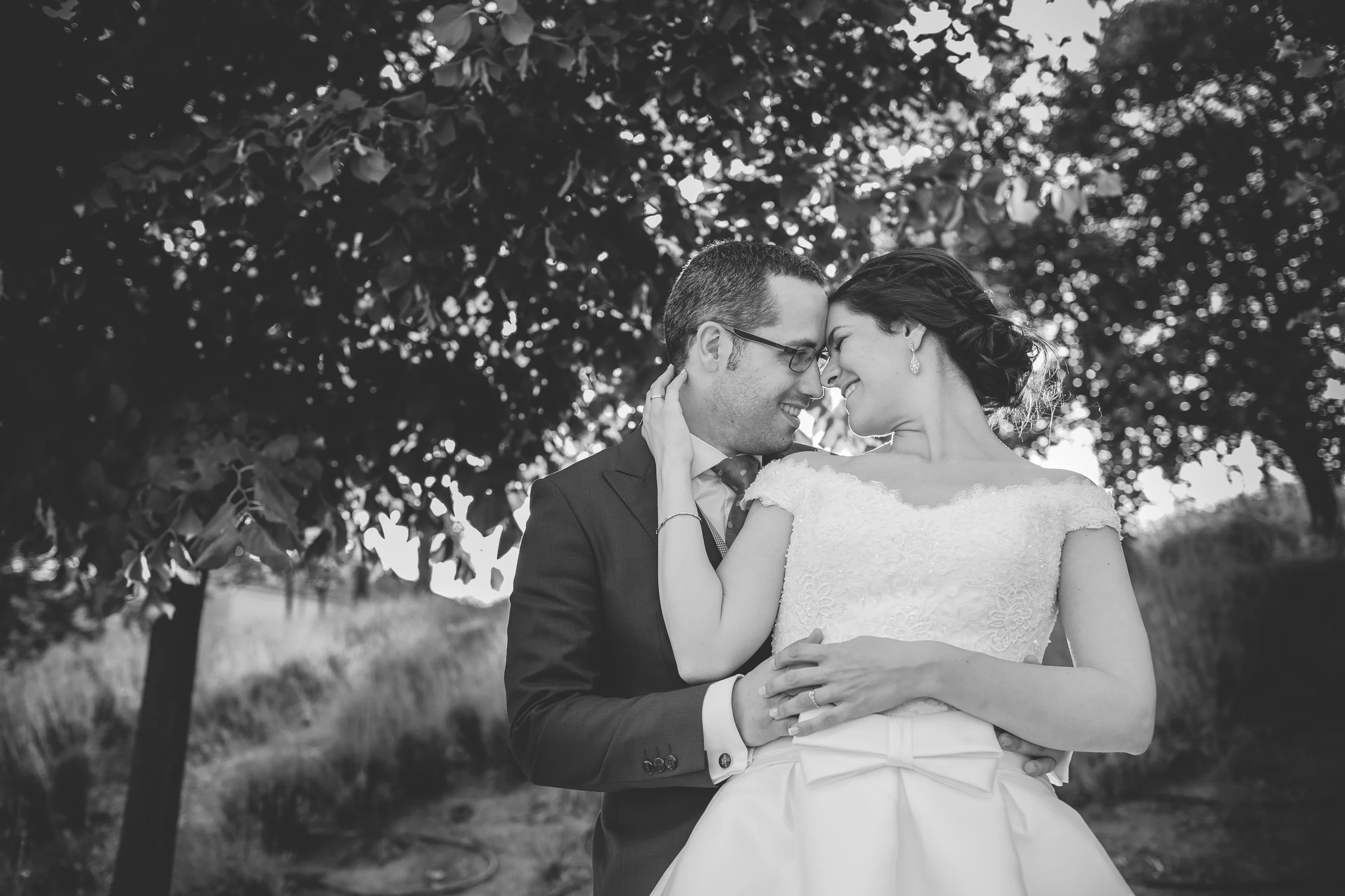 Retrato en blanco y negro de una pareja abrazada bajo los árboles.