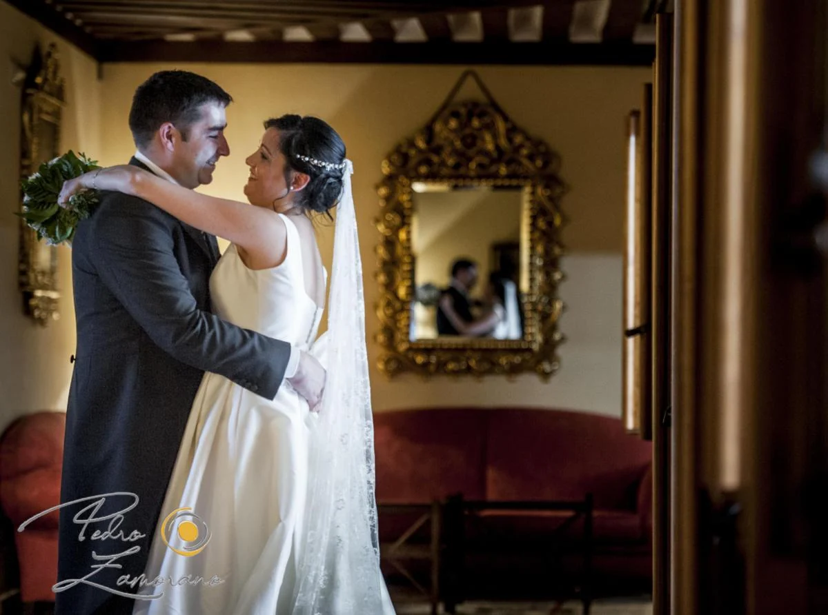 Novios abrazados en un salón con espejo dorado de El Antiguo Convento.
