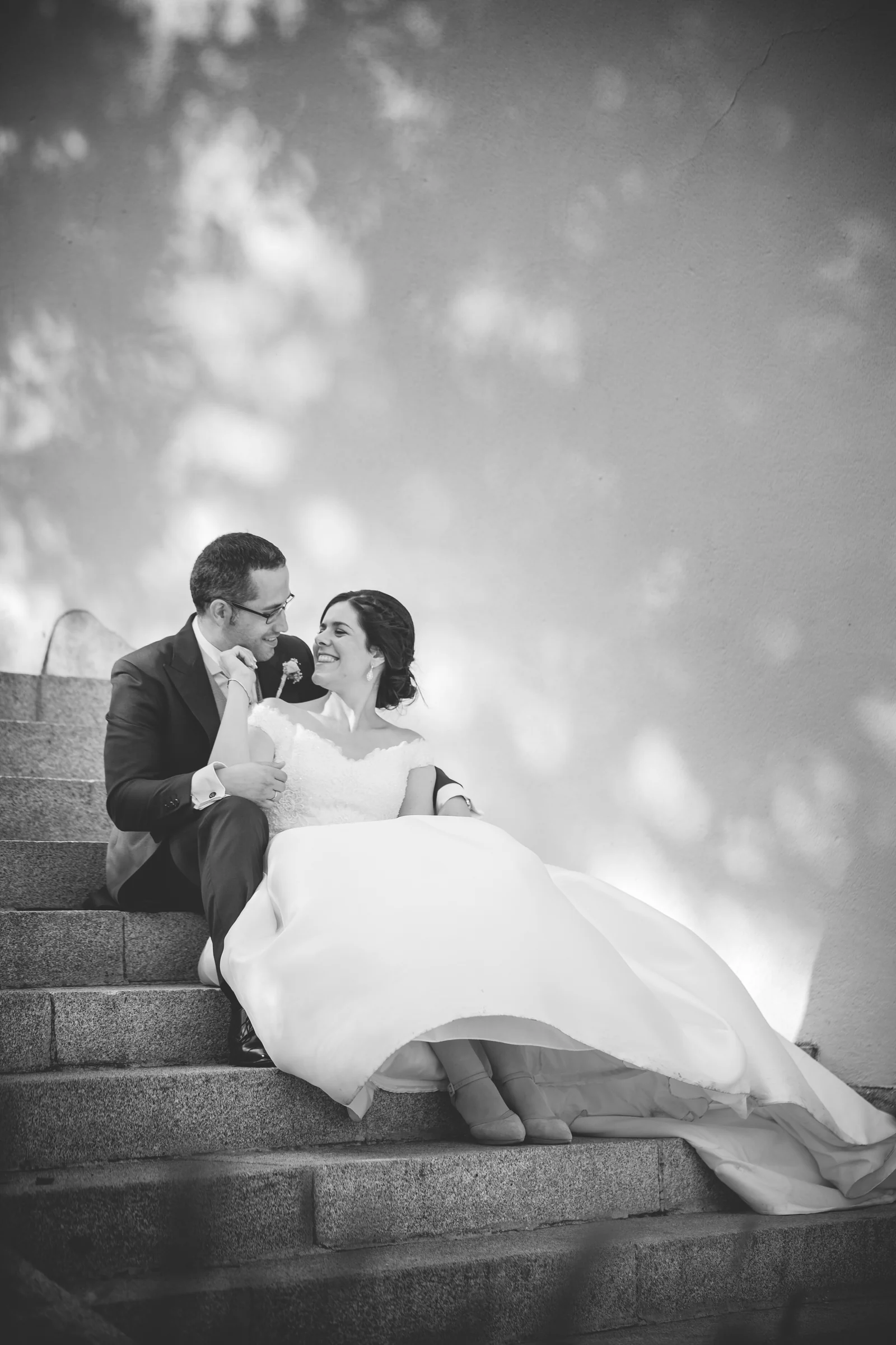 Novios sentados juntos en una escalera y sonriendo en blanco y negro.