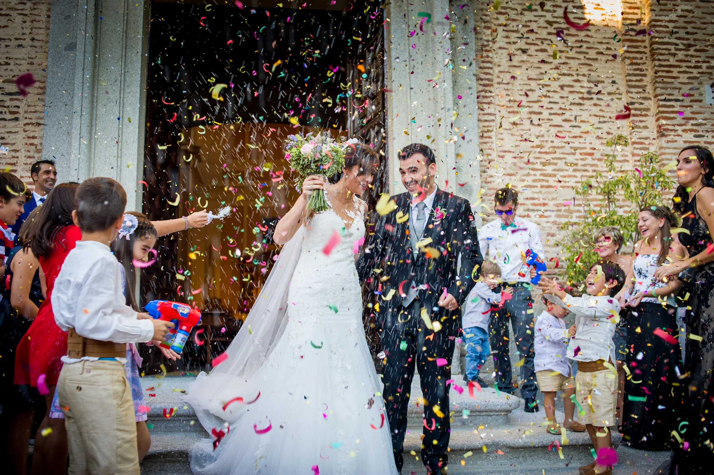 Novios saliendo de la ceremonia bajo una lluvia de confeti de colores.