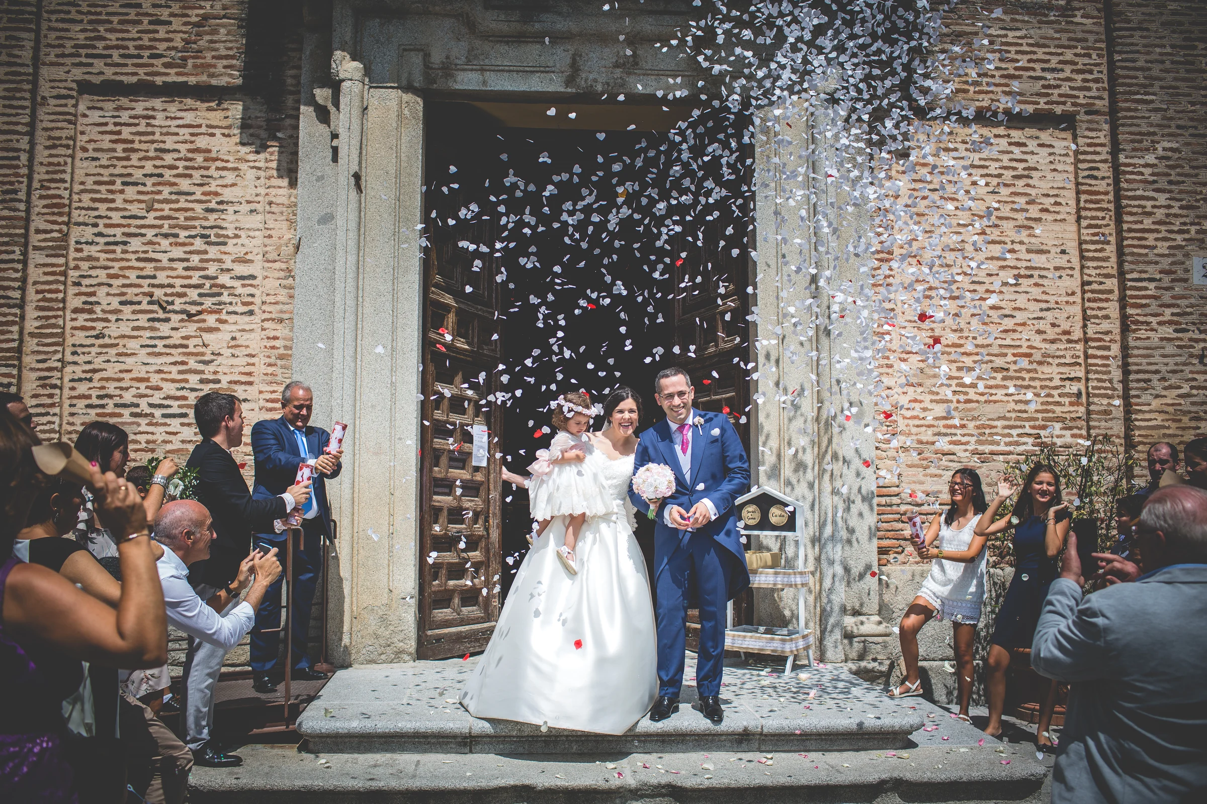 Novios saliendo de la ceremonia bajo una lluvia de pétalos blancos.