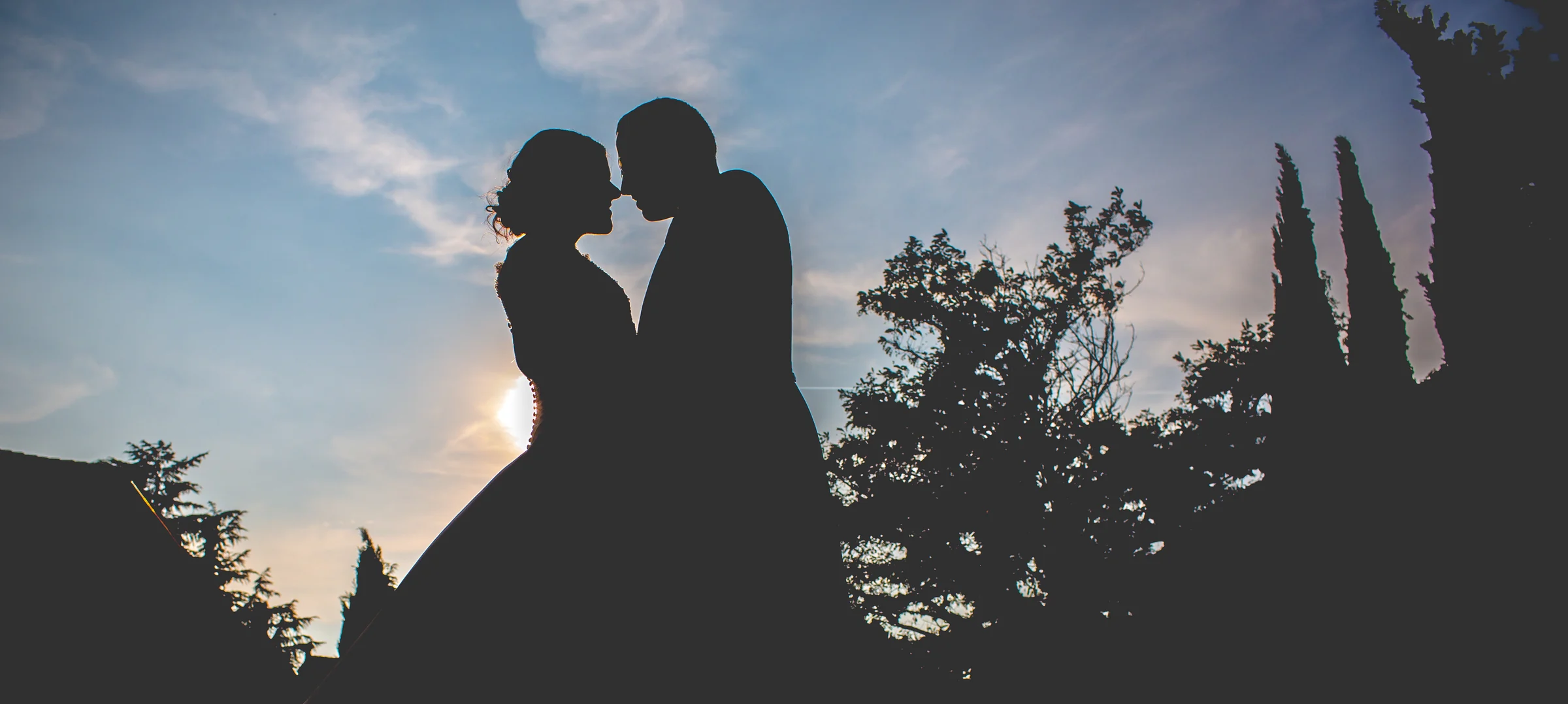 Silueta de una pareja de novios frente al cielo y el sol de la tarde.