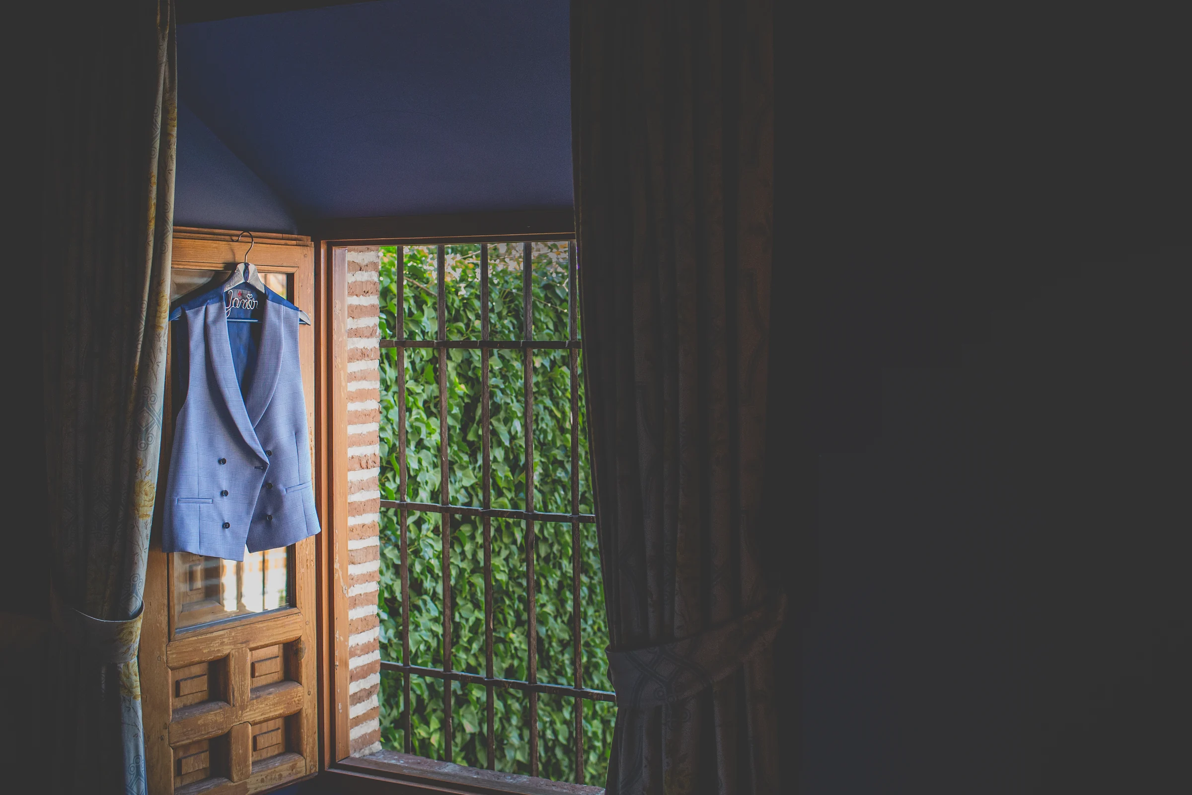 Vestido de novia colgado junto a una ventana de madera antes de la boda.