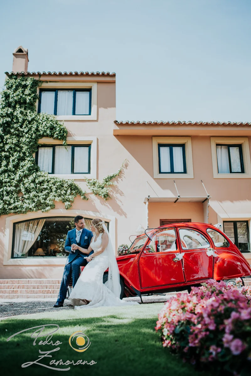 Novios junto a un coche clásico rojo en Finca La Alquería