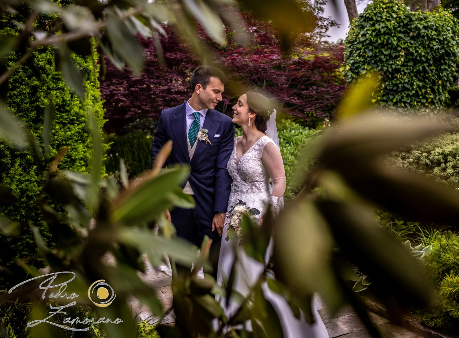Pareja fotografiada entre hojas y vegetación en los jardines de Hacienda Jacaranda.