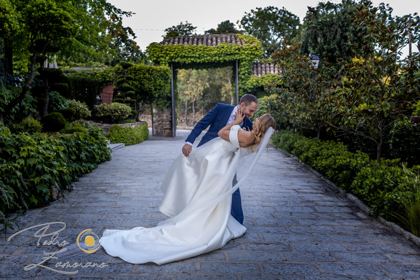 Pareja de novios en una pose de beso sobre un camino de piedra en los jardines de Hacienda Jacaranda.