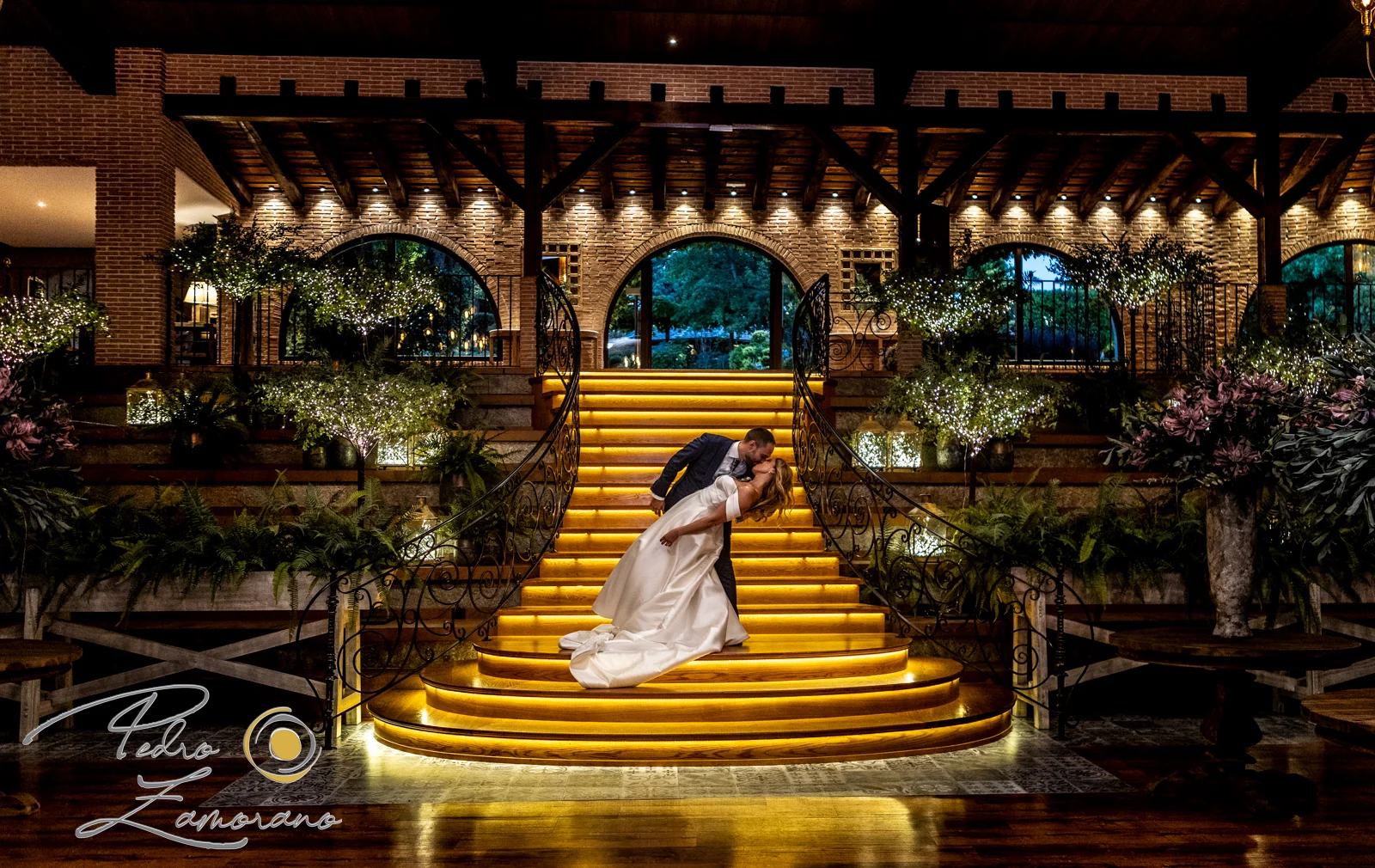 Novios besándose sobre la escalera iluminada de Hacienda Jacaranda durante la noche.