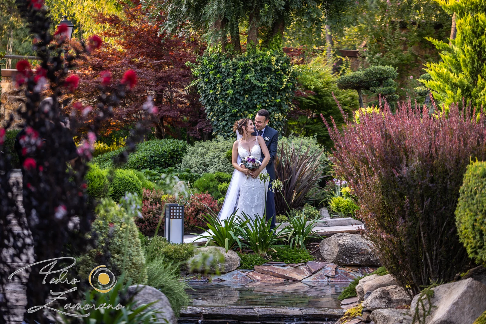 Pareja abrazada entre la vegetación y el estanque de los jardines de Hacienda Jacaranda.