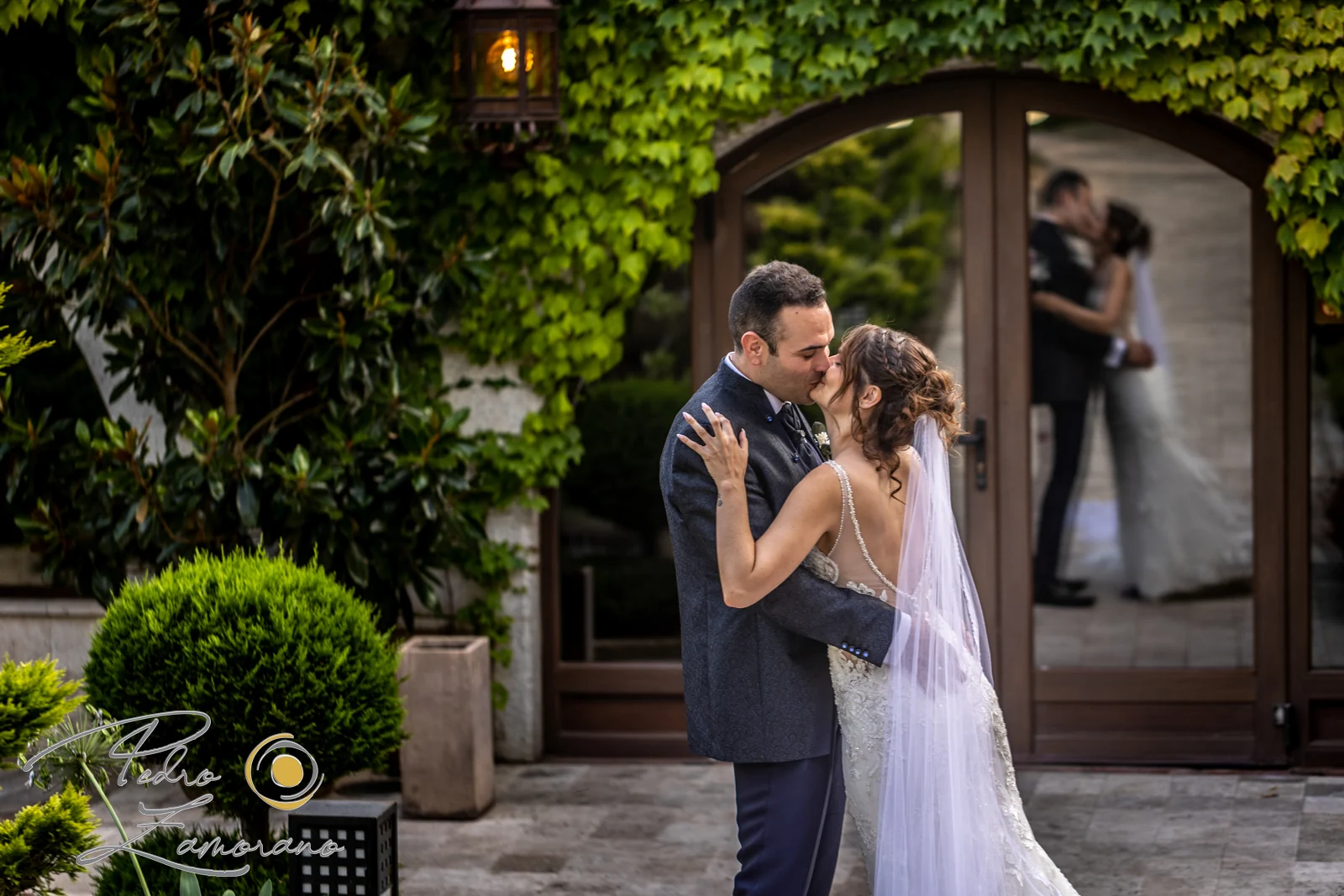 Novios besándose con su reflejo visible en una puerta acristalada de Hacienda Jacaranda.