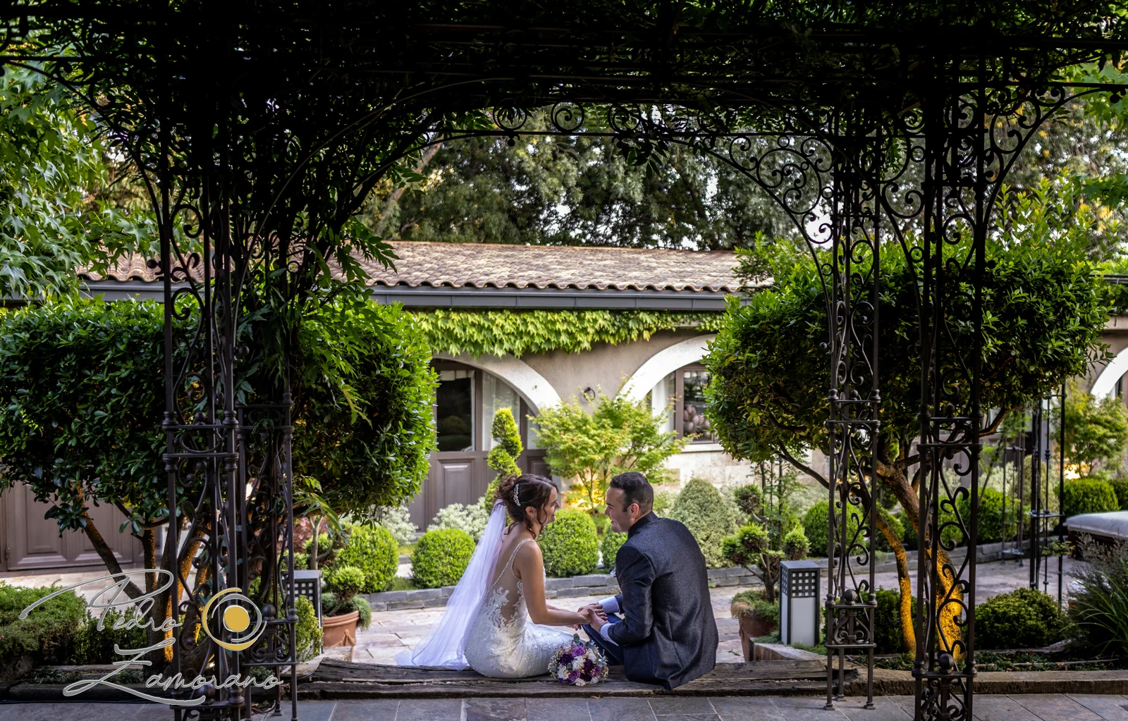 Pareja sentada bajo una estructura de hierro rodeada de vegetación en Hacienda Jacaranda.