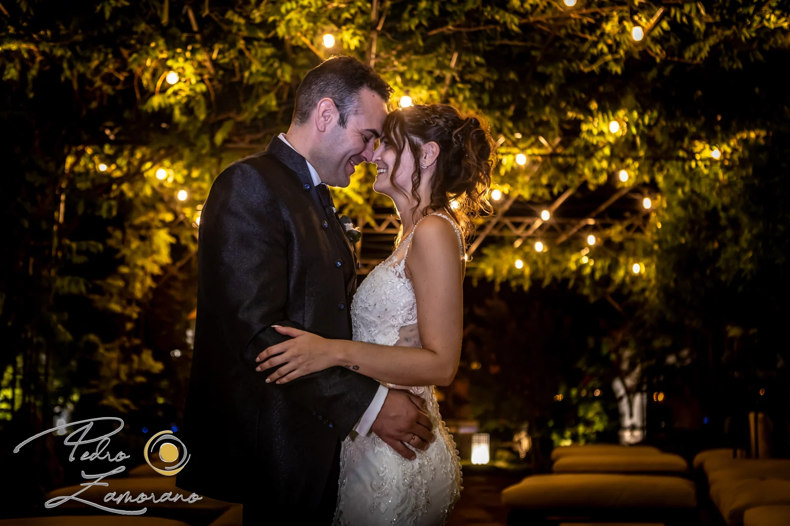 Pareja de novios retratada de noche bajo luces cálidas en los jardines de Hacienda Jacaranda.
