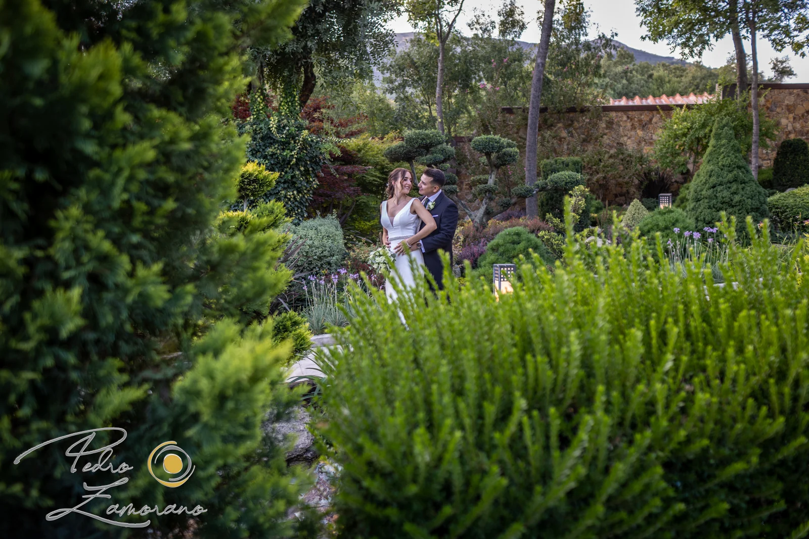 Pareja fotografiada a distancia entre la abundante vegetación de los jardines de Hacienda Jacaranda.