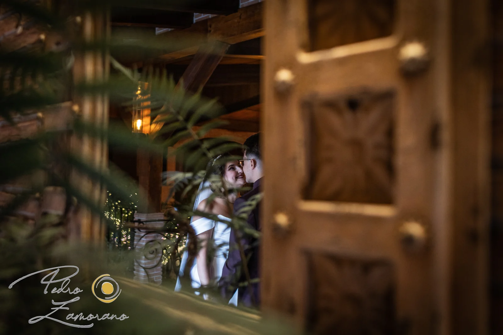 Mirada de una pareja fotografiada entre hojas y elementos de madera en Hacienda Jacaranda.