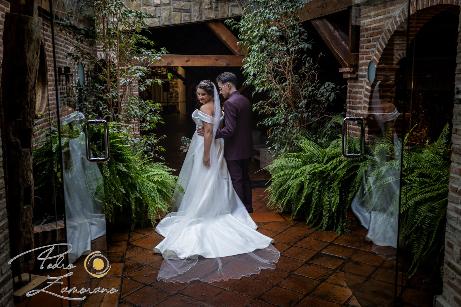 Novios posando en la entrada de un patio de ladrillo y helechos de Hacienda Jacaranda.