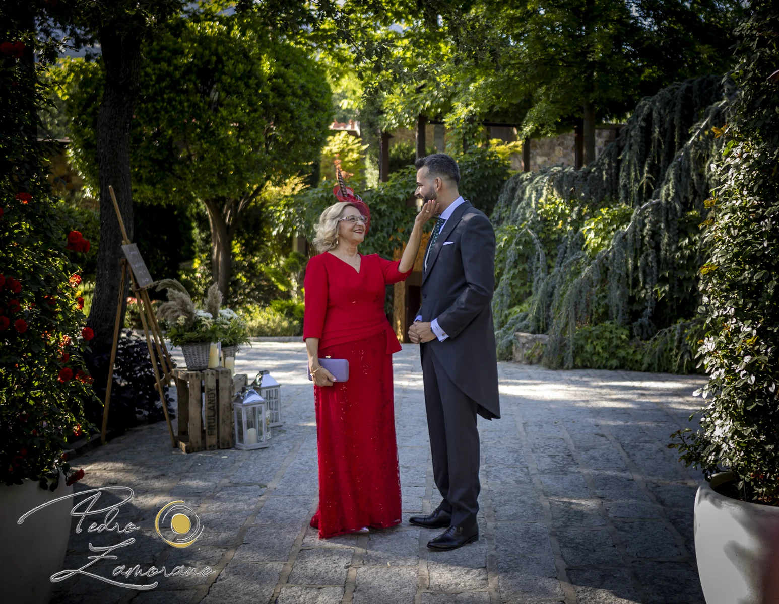Momento familiar entre un hombre vestido de ceremonia y una mujer con vestido rojo en los jardines de Hacienda Jacaranda.