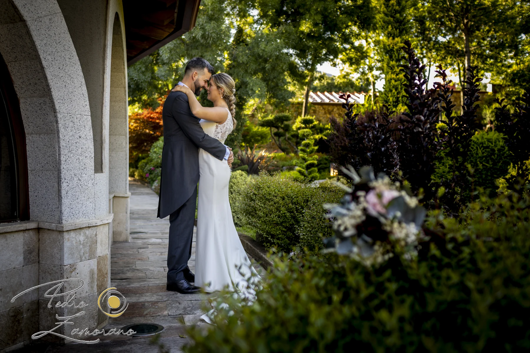 Novios abrazados junto a la arquitectura y los jardines de Hacienda Jacaranda.