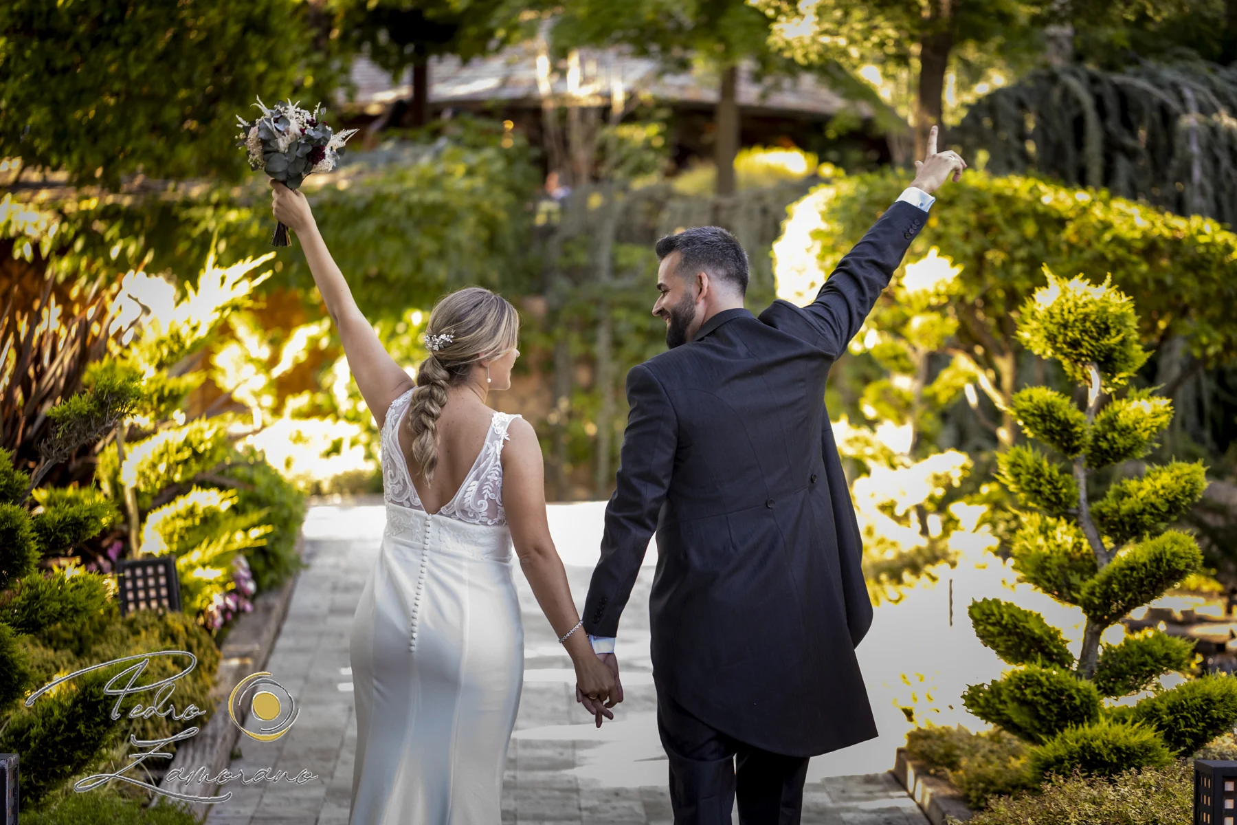 Pareja caminando de la mano con los brazos levantados por los jardines de Hacienda Jacaranda.