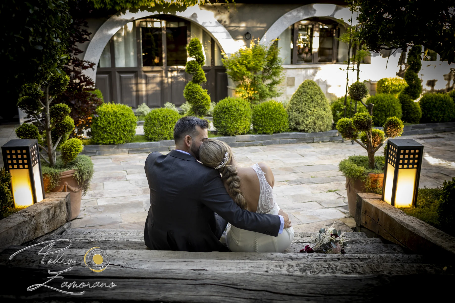 Novios sentados juntos en unos escalones de madera dentro de los jardines de Hacienda Jacaranda.