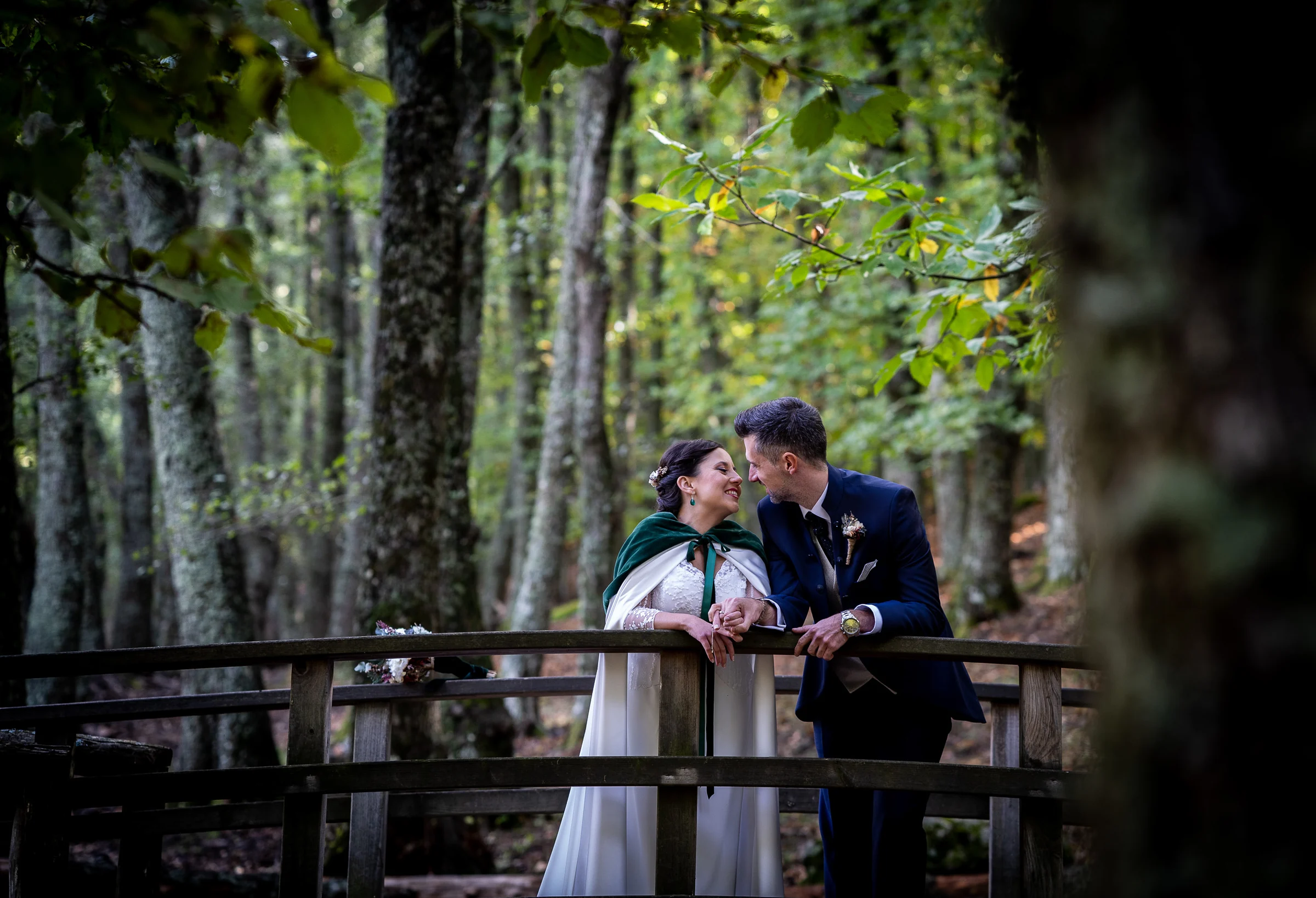 Idoya y Daniel se abrazan sobre un puente de madera rodeado de vegetación durante su postboda en El Tiemblo.