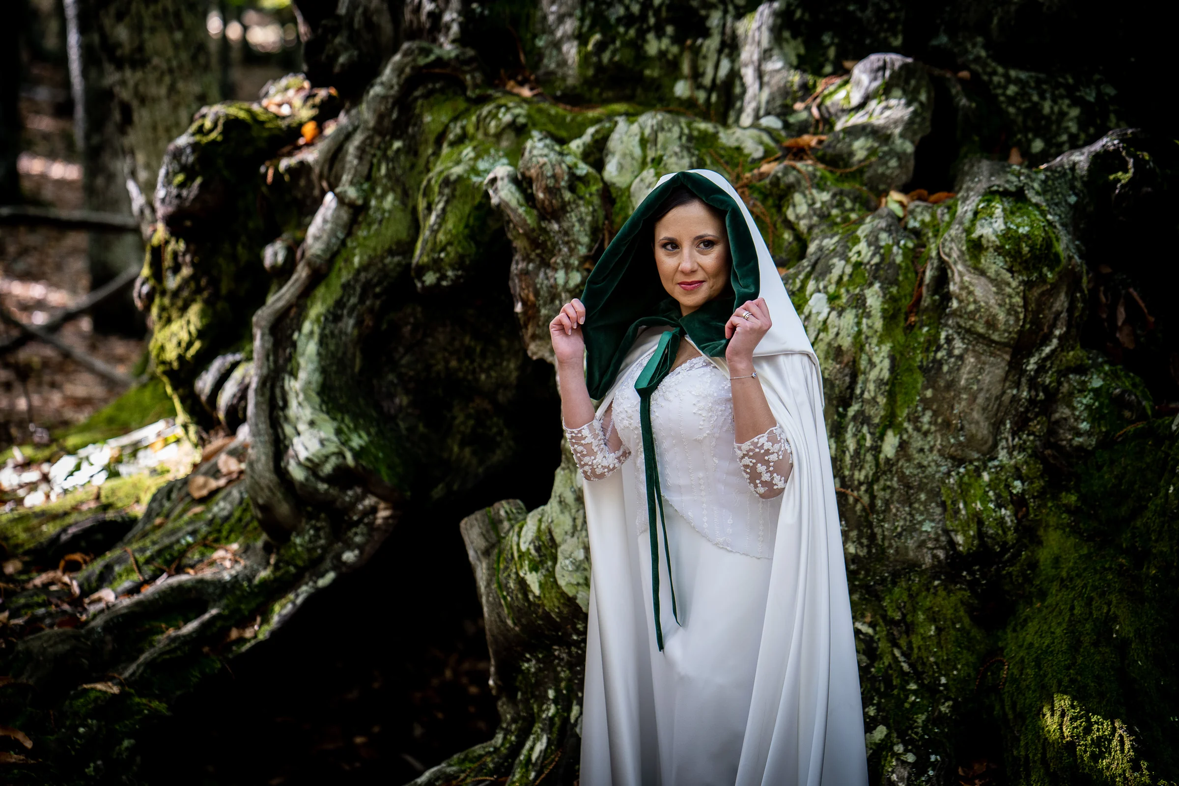 Retrato de Idoya con una capa de capucha verde junto a las raíces de un gran castaño en El Tiemblo.