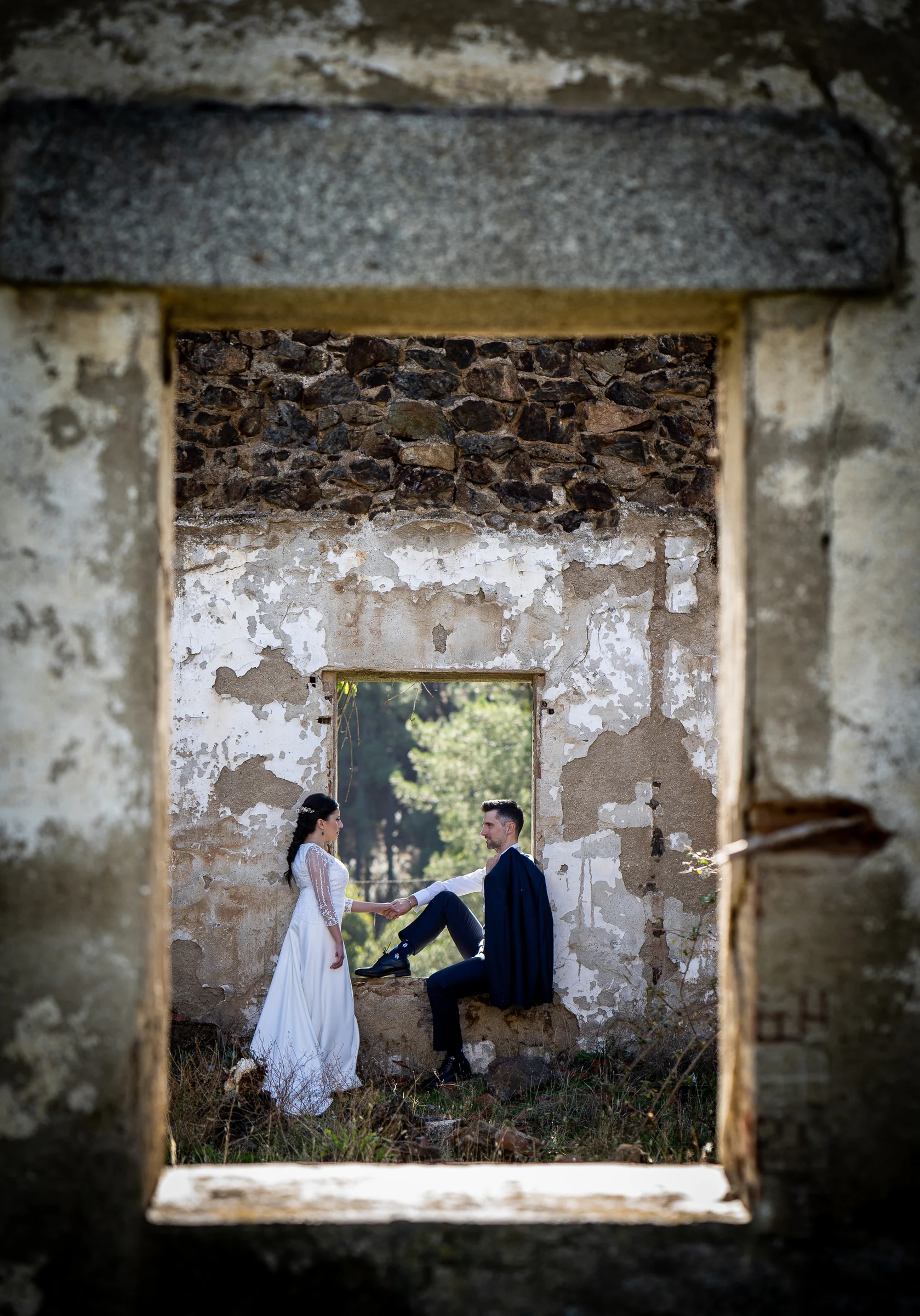 Idoya toma la mano de Daniel sentado en el hueco de una ventana dentro de un edificio en ruinas durante su postboda en El Tiemblo.