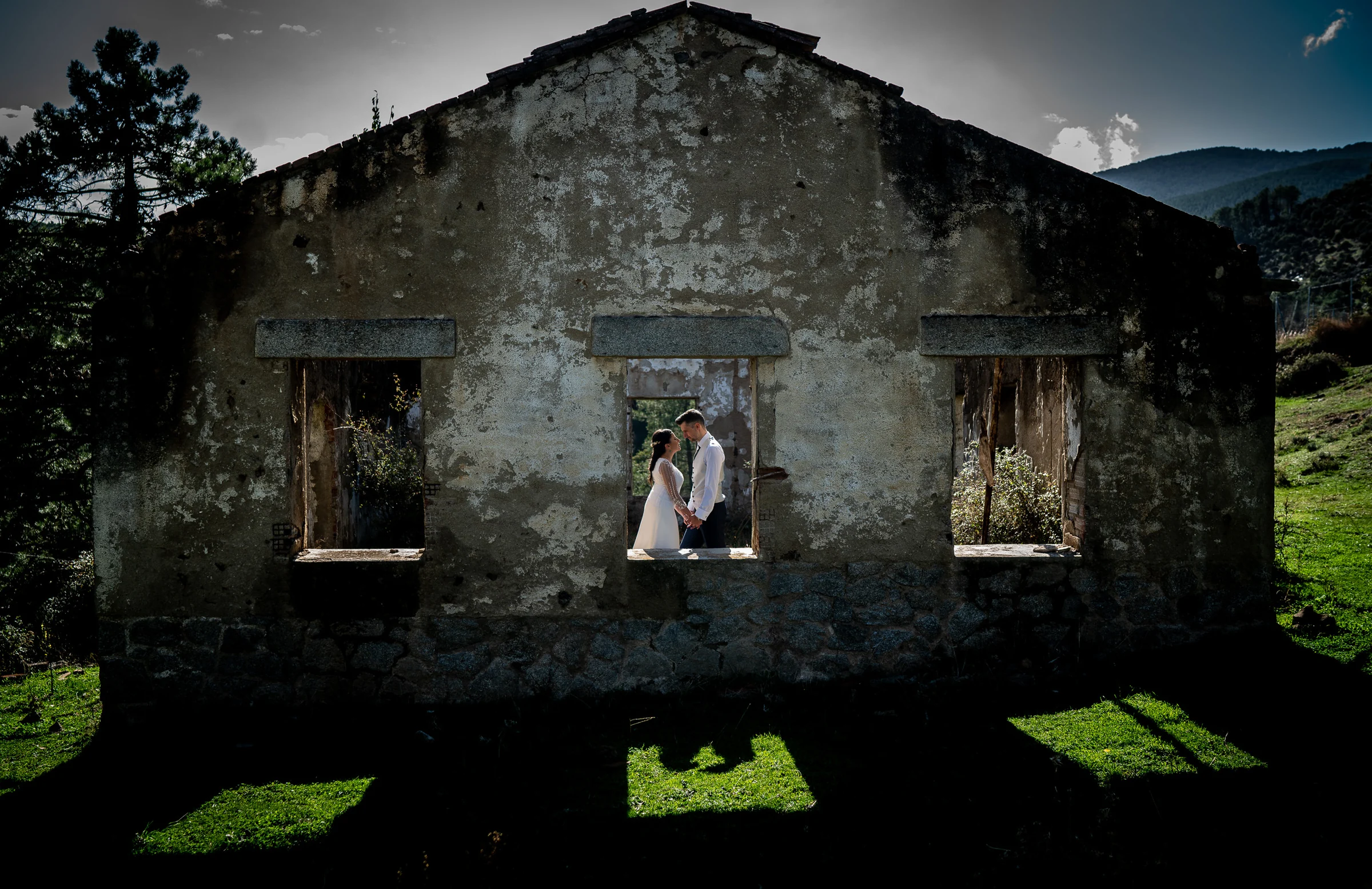 Idoya y Daniel se acercan en la ventana central de una fachada abandonada durante su postboda en el entorno de El Tiemblo.