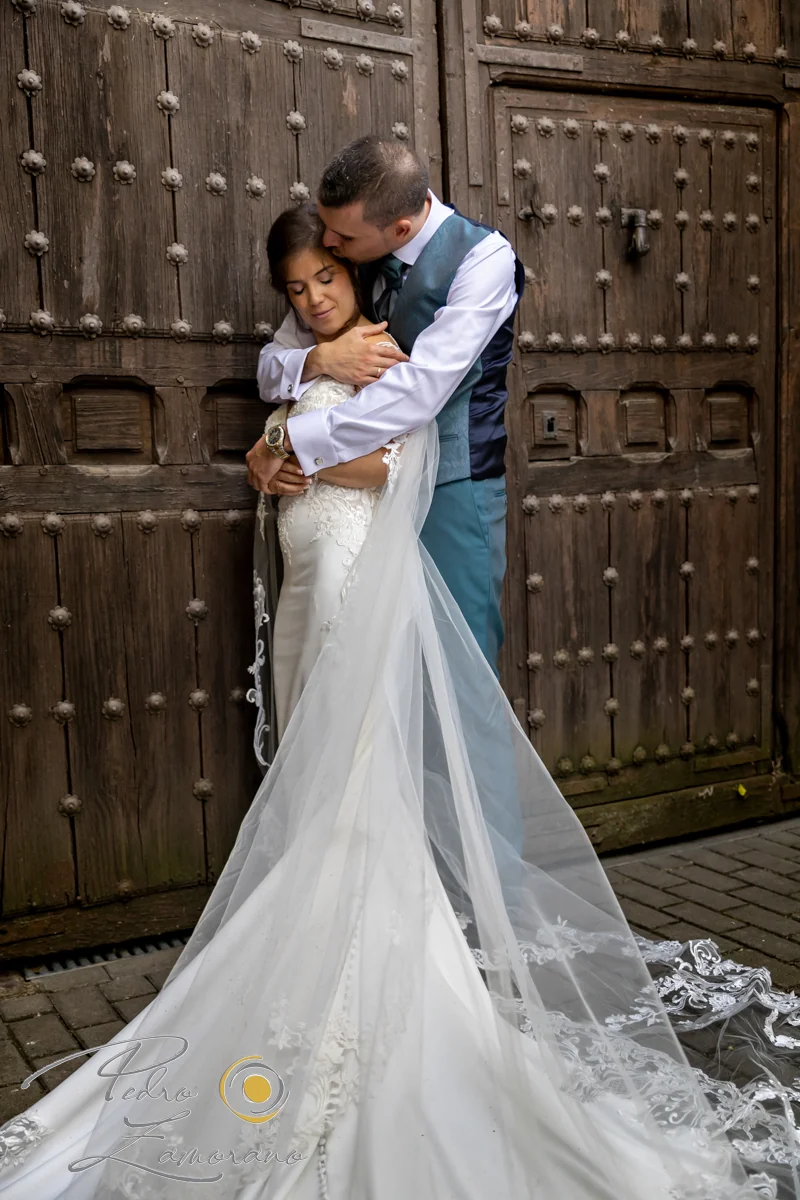 Novios abrazados frente a una gran puerta de madera rústica durante su boda en Jardín El Botero.