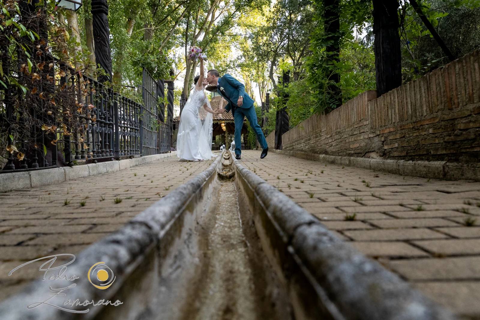 Novios besándose al fondo de un paseo con canal de agua entre los jardines de Jardín El Botero.