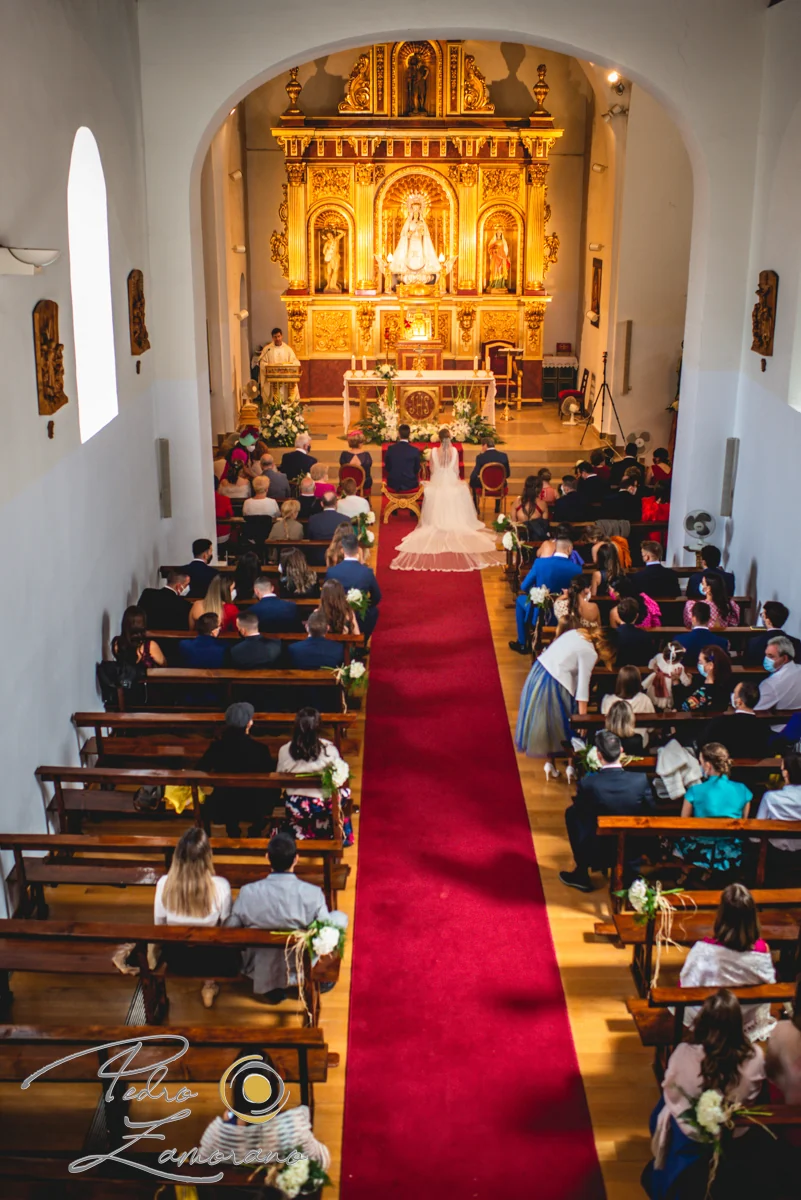 Vista general de una ceremonia de boda en la iglesia con los novios frente al altar y los invitados en los bancos.