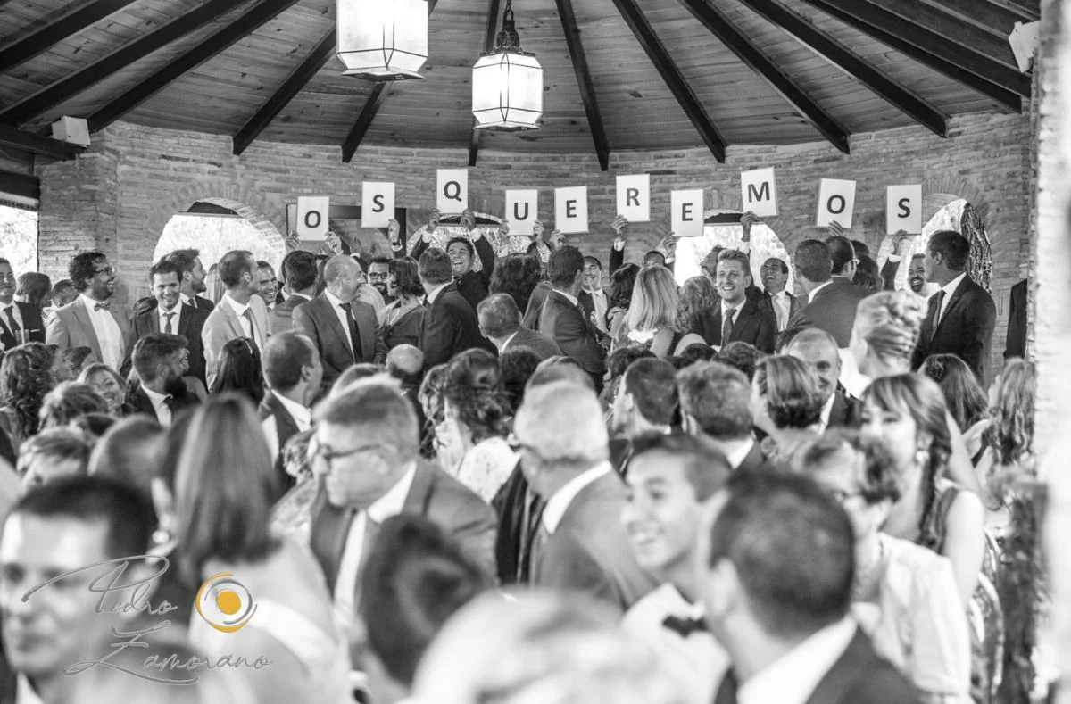Grupo de invitados levantando carteles con el mensaje Os queremos durante el banquete de una boda en Jardín El Botero.