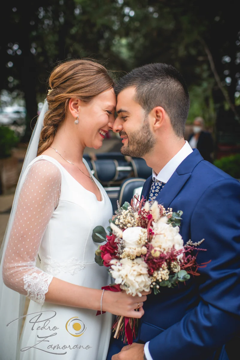 Retrato cercano de los novios sonriendo frente a frente con el ramo de la novia en Jardín El Botero.