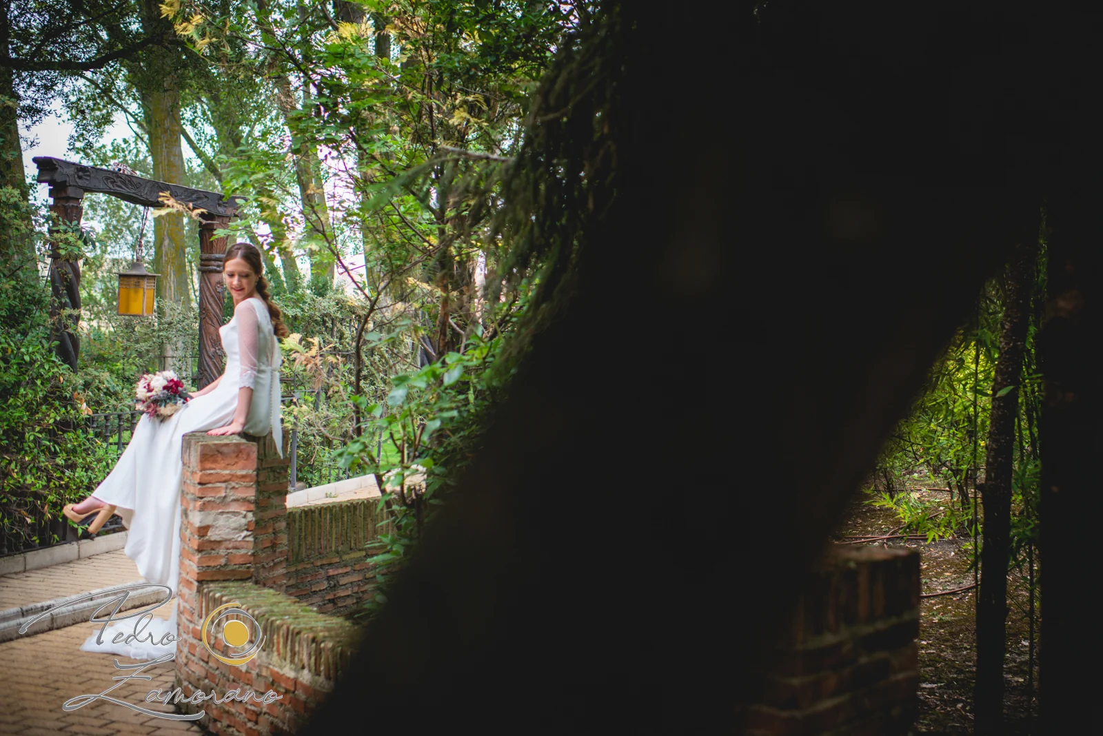 Novia sentada en un rincón de ladrillo y vegetación dentro de los jardines de Jardín El Botero.