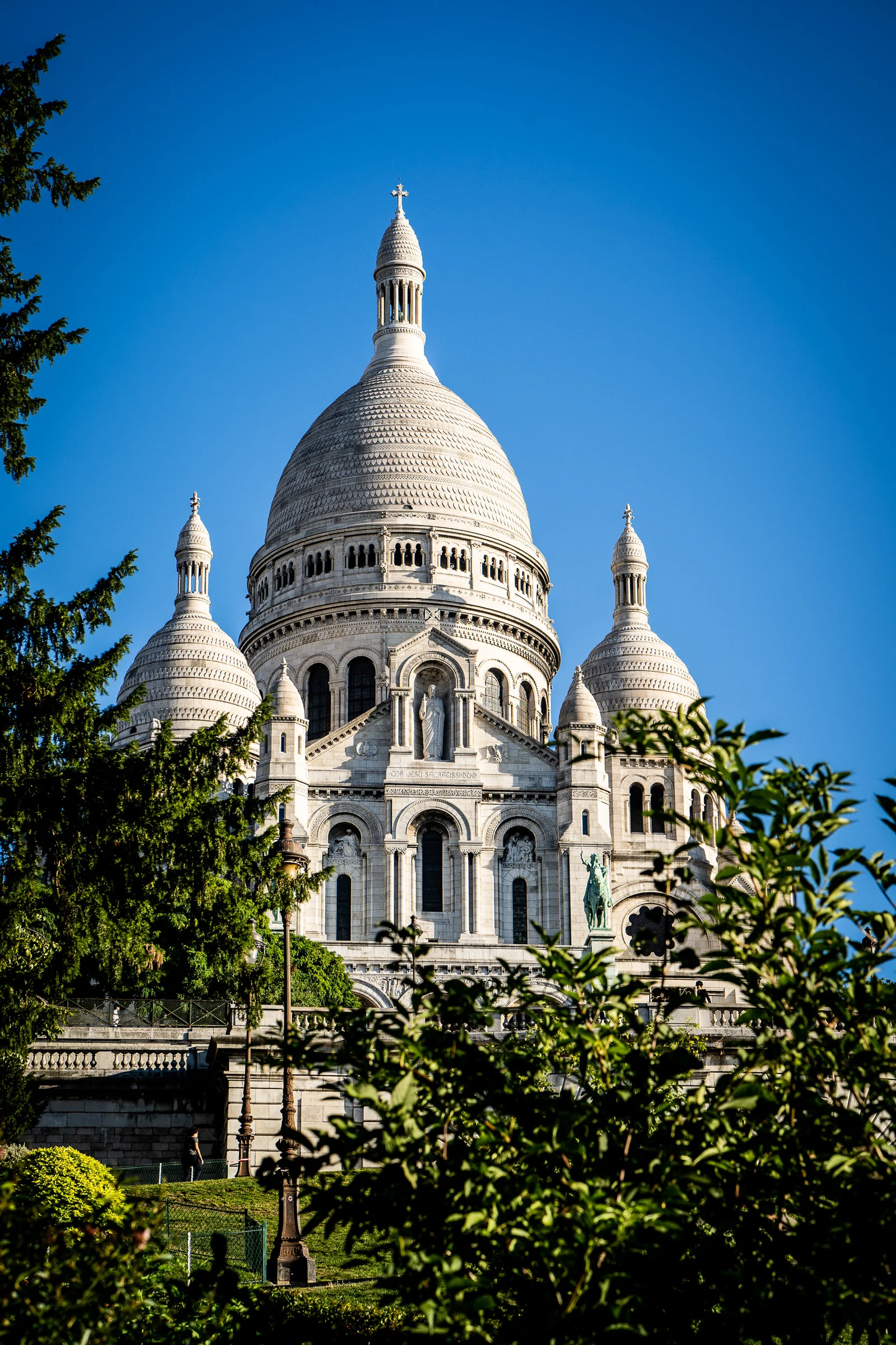 Vista vertical de la basílica del Sacré-Cœur en Montmartre bajo un cielo azul intenso.